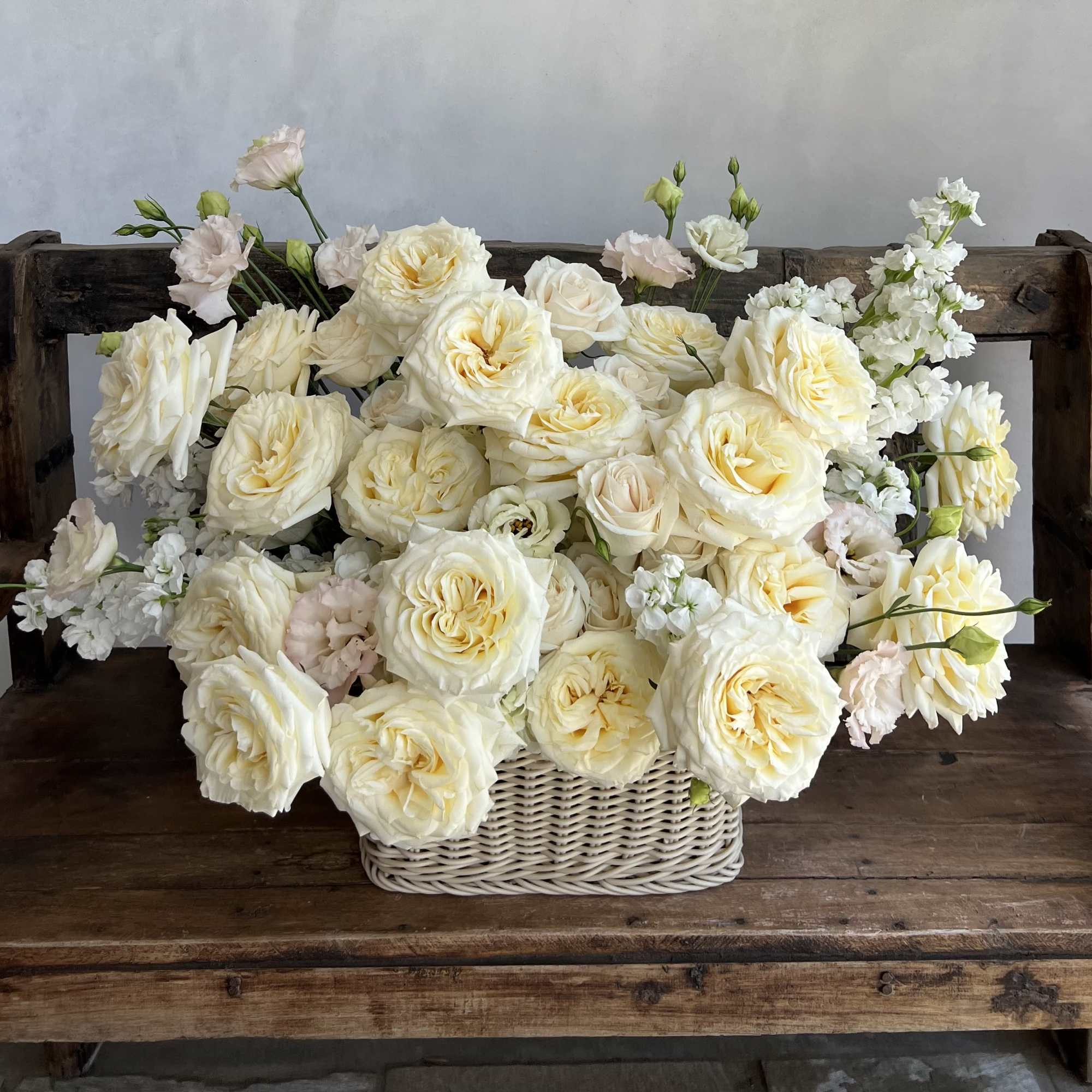 Cream roses and white blooms arranged in a wicker basket