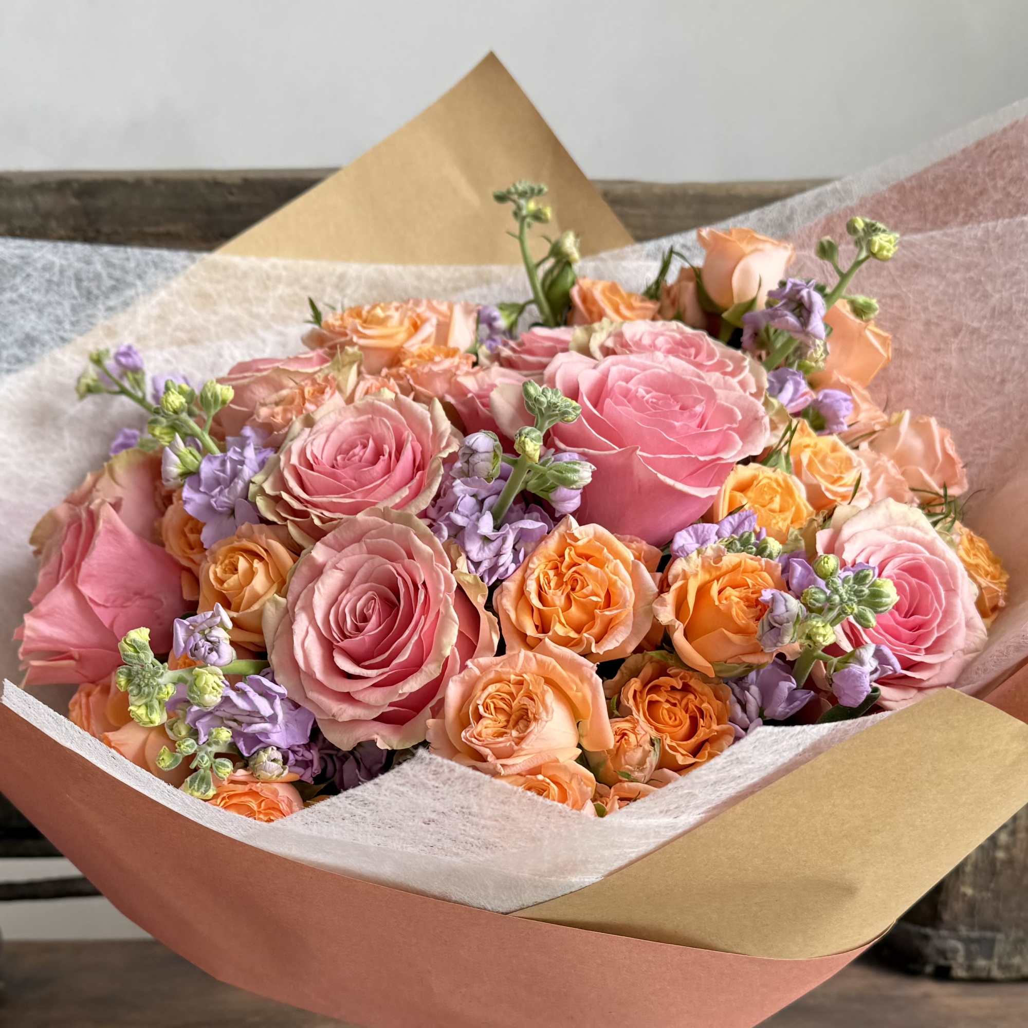 Bouquet of pink and peach roses with lavender flowers in paper wrap