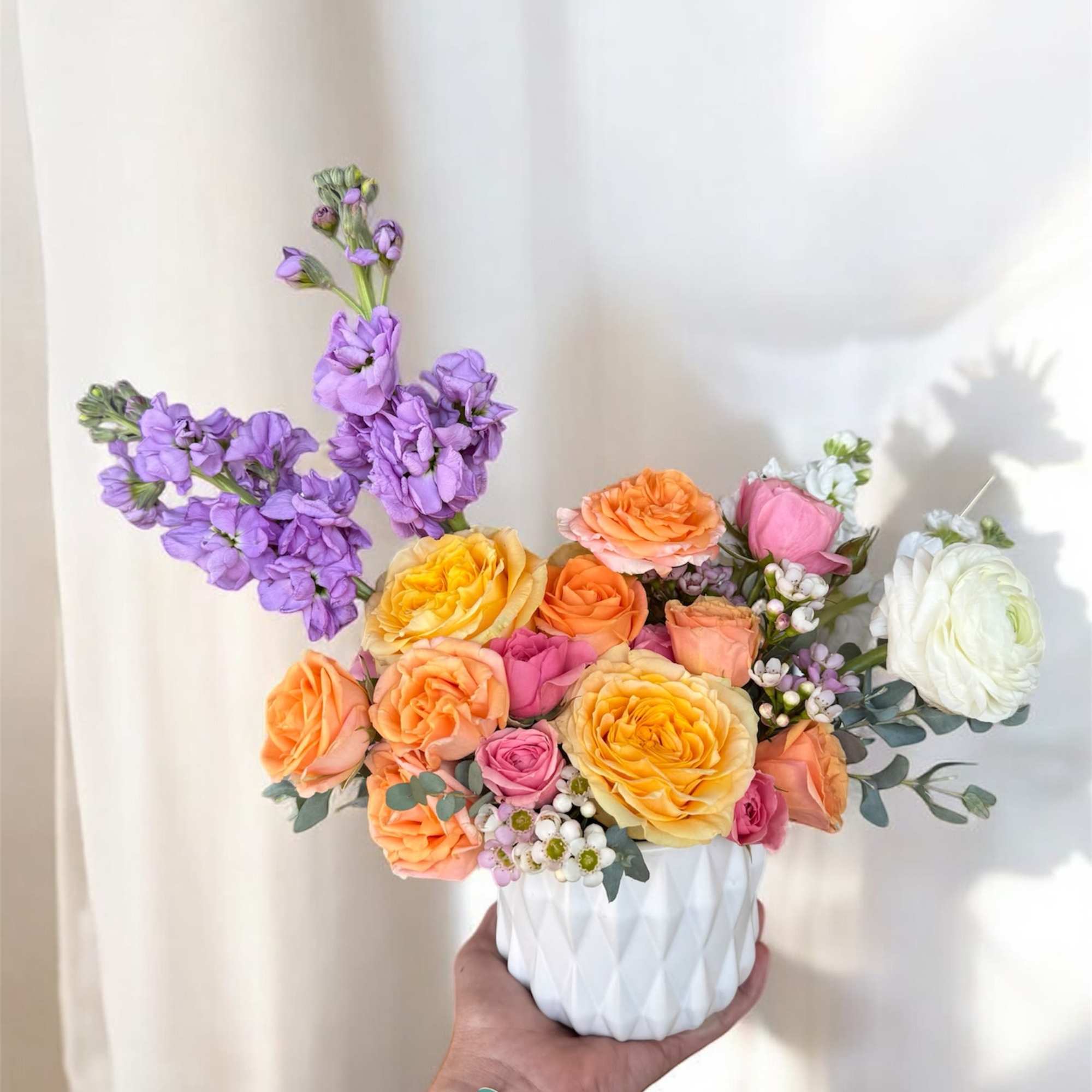 Colorful bouquet of roses and purple flowers in a white vase