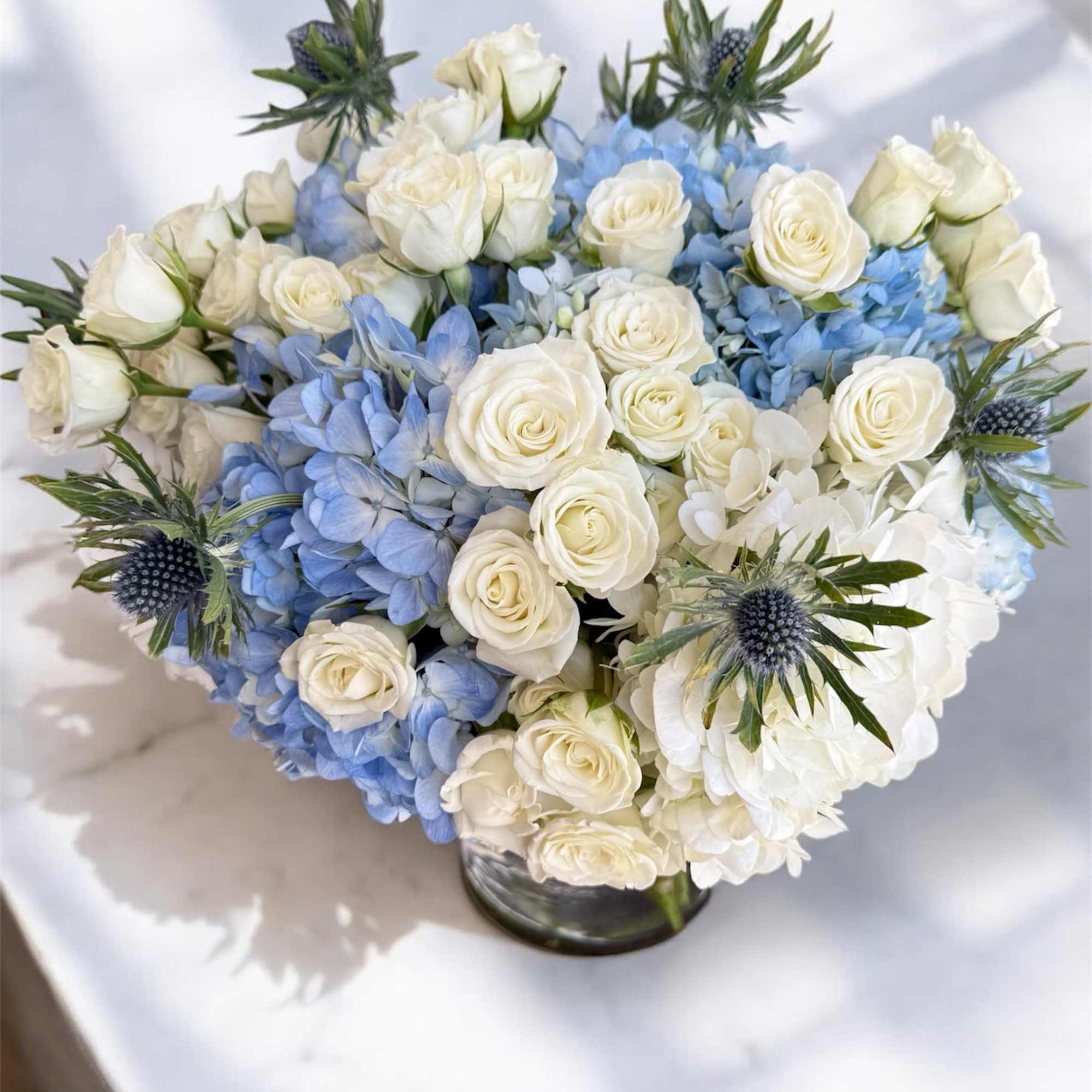 White roses and blue hydrangeas in a low glass vase