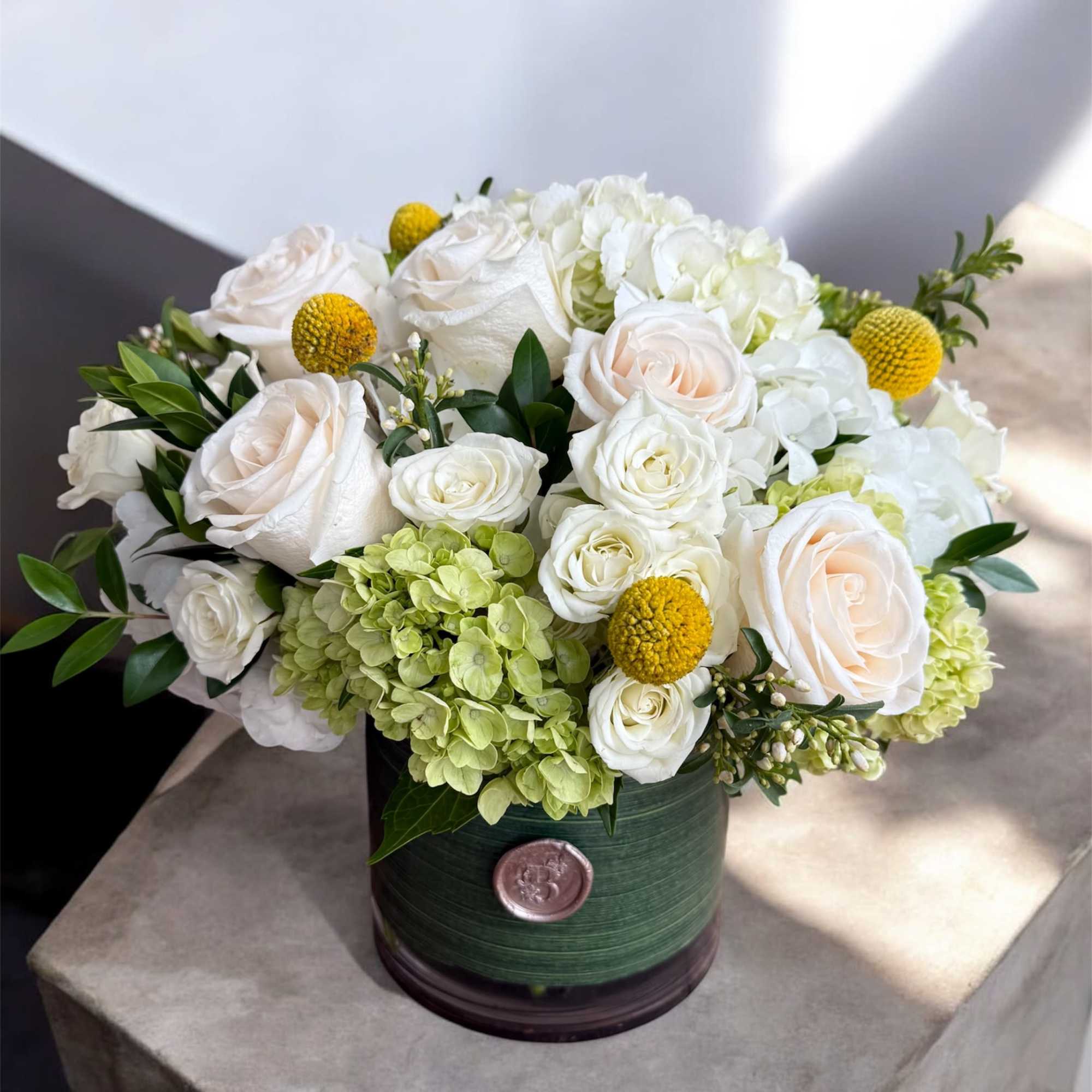 White roses and hydrangeas in a green round box with yellow accents