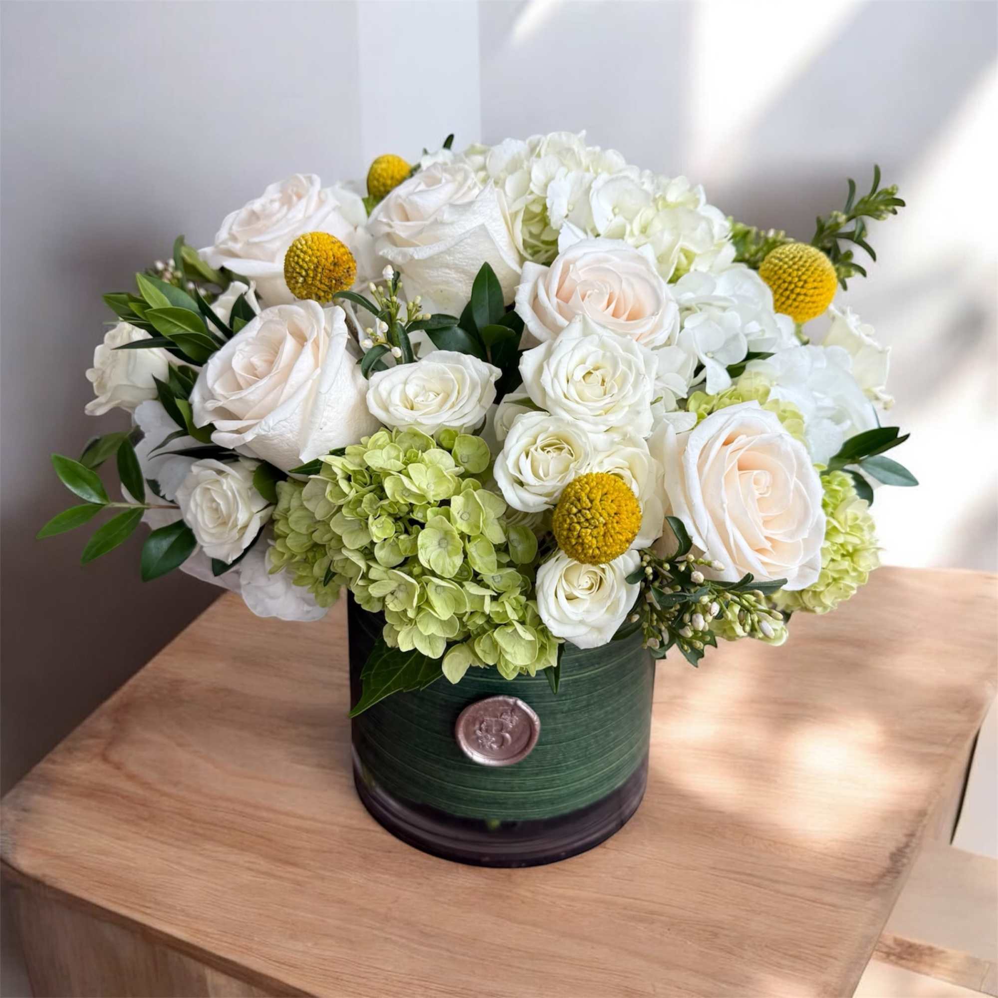 White roses and hydrangeas in a green hatbox with yellow accents