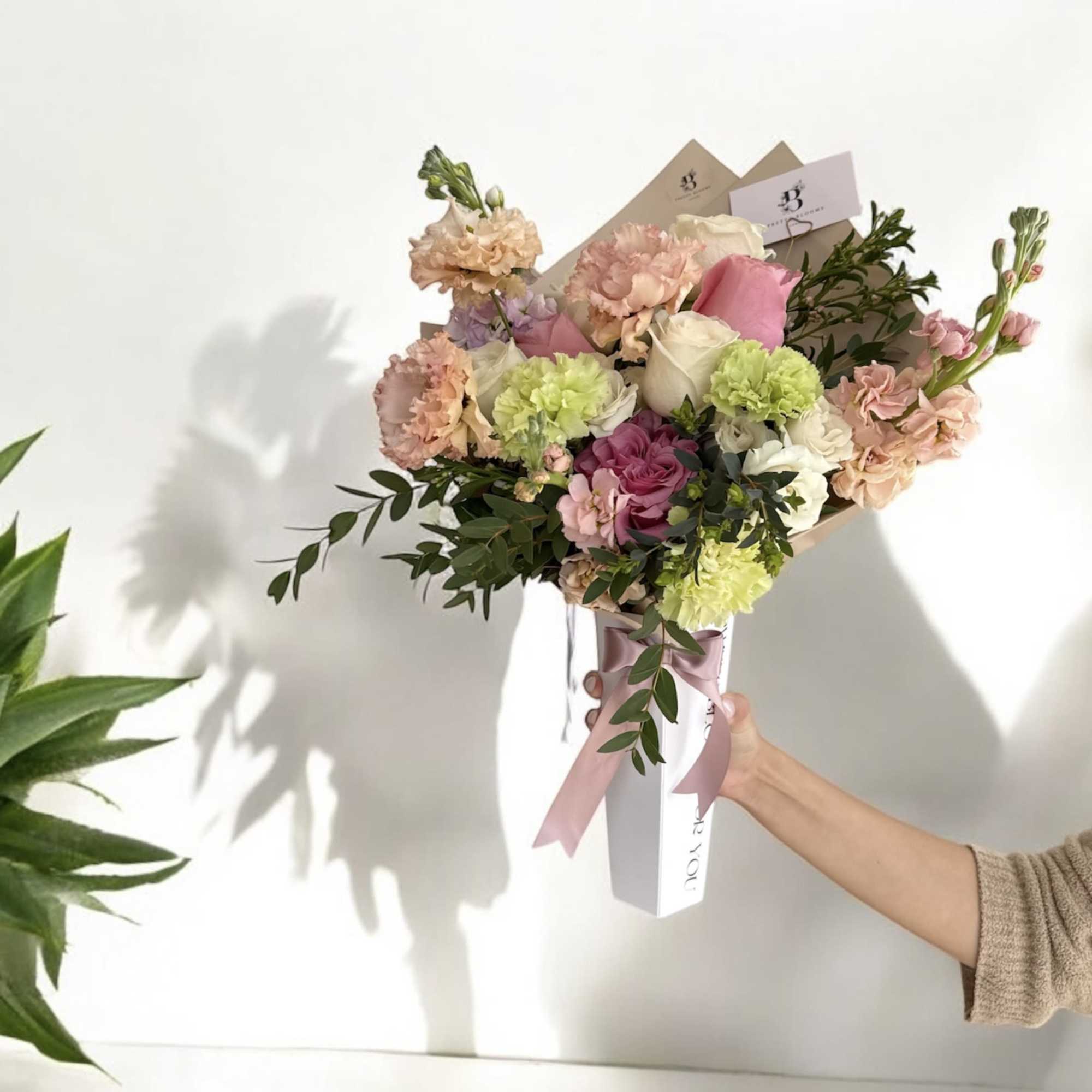 Handheld bouquet of pink, cream, and green flowers wrapped in paper