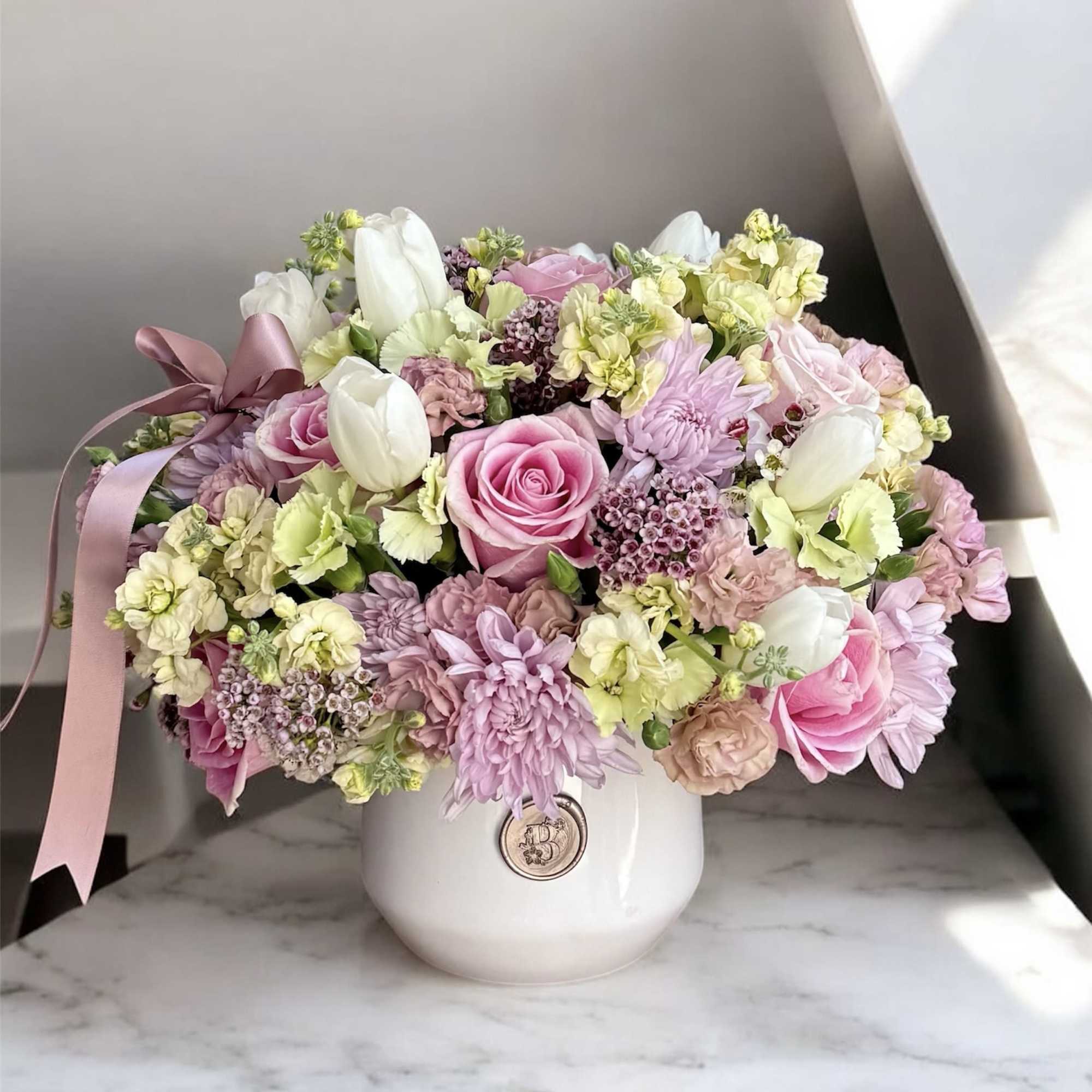 Pink and white mixed flower arrangement in a white vase with a ribbon