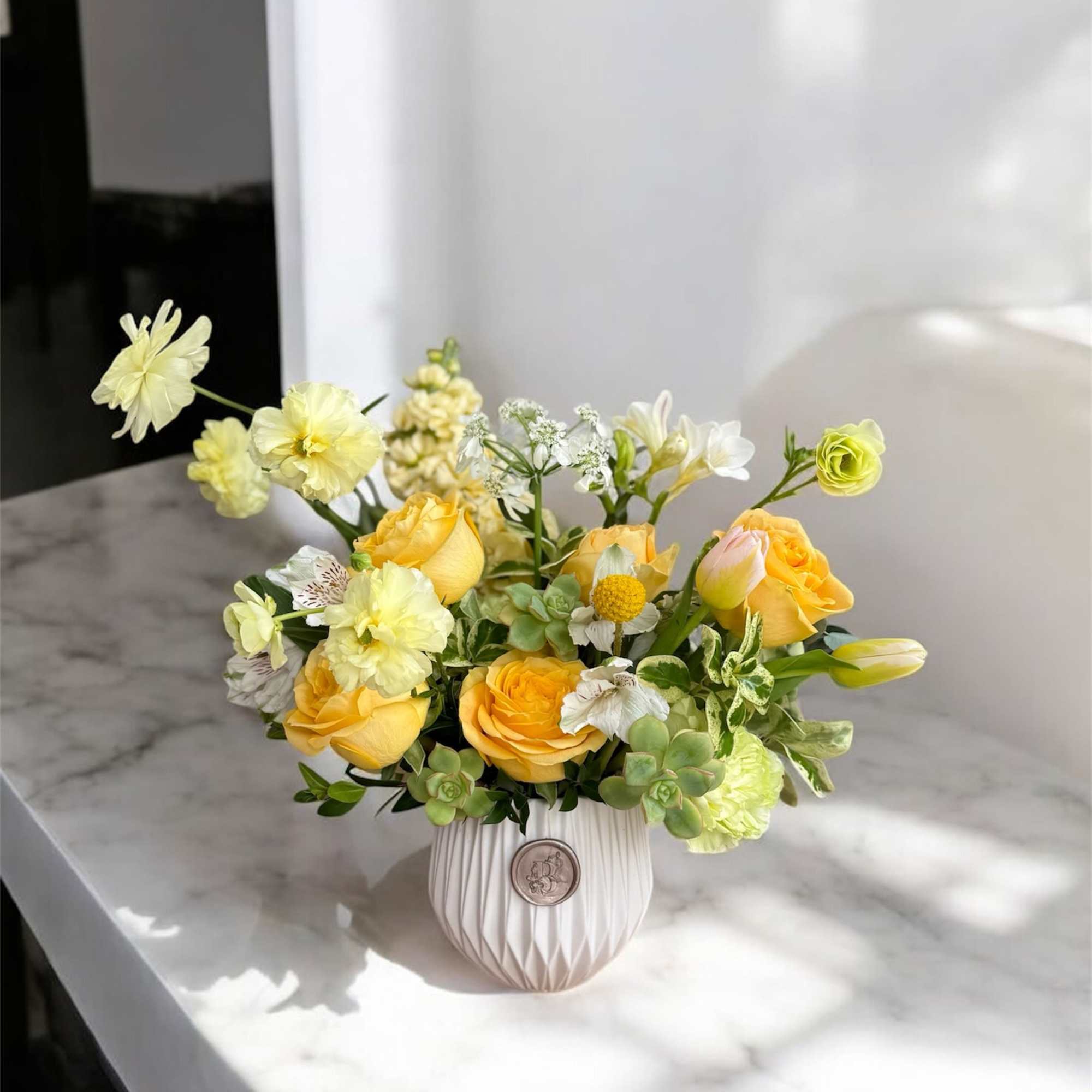 Yellow roses and white flowers arranged in a white vase