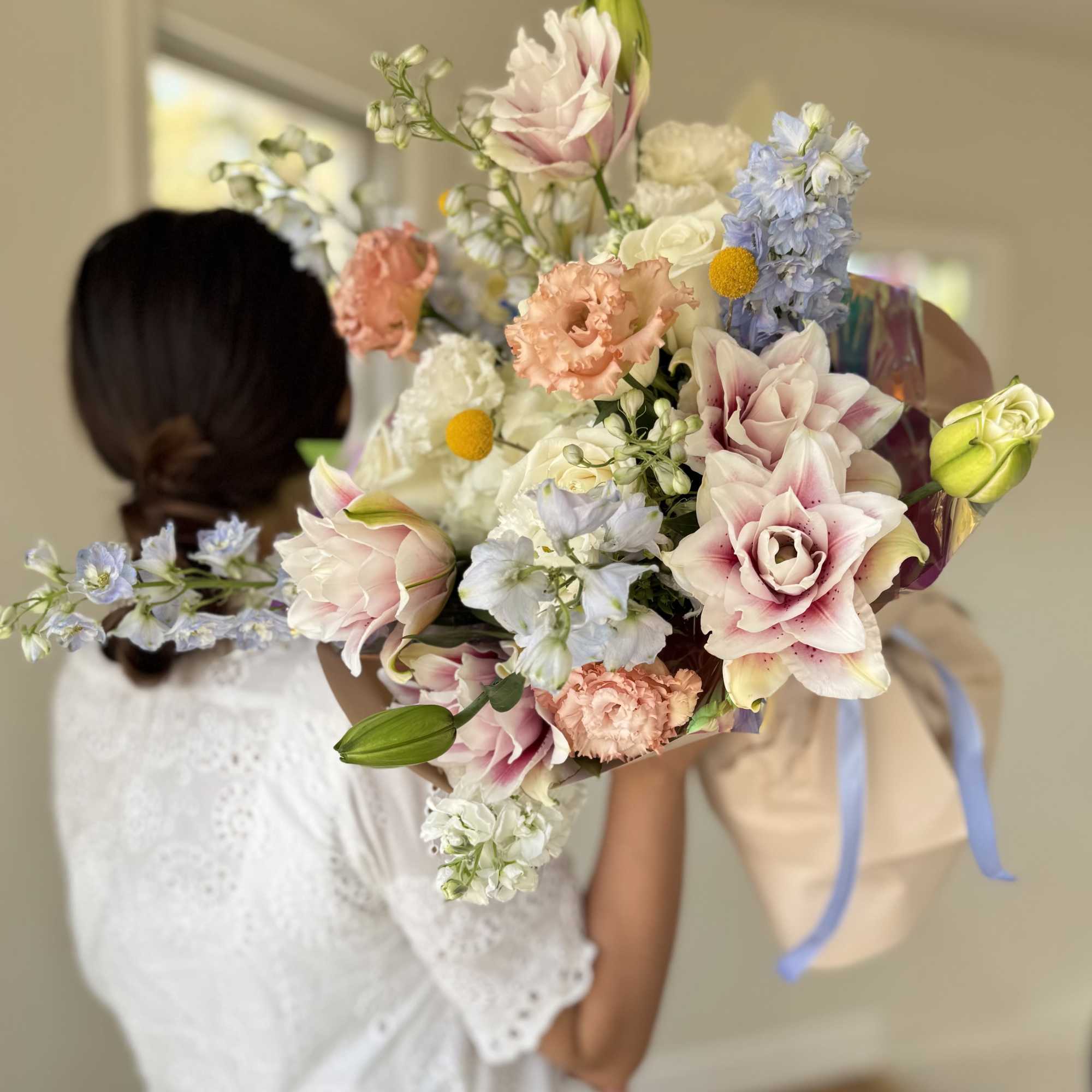 Bride holding a pastel bouquet with lilies, roses, and blue flowers