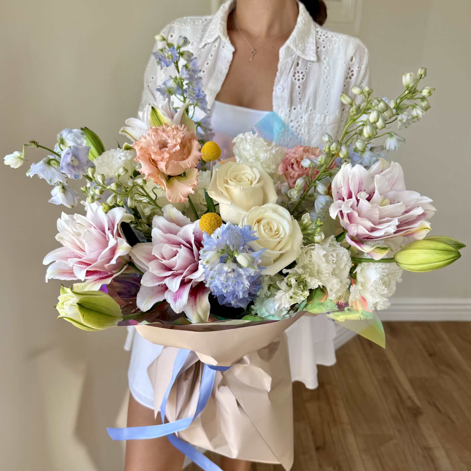 Large pastel bouquet with roses, lilies, and mixed blooms wrapped in paper