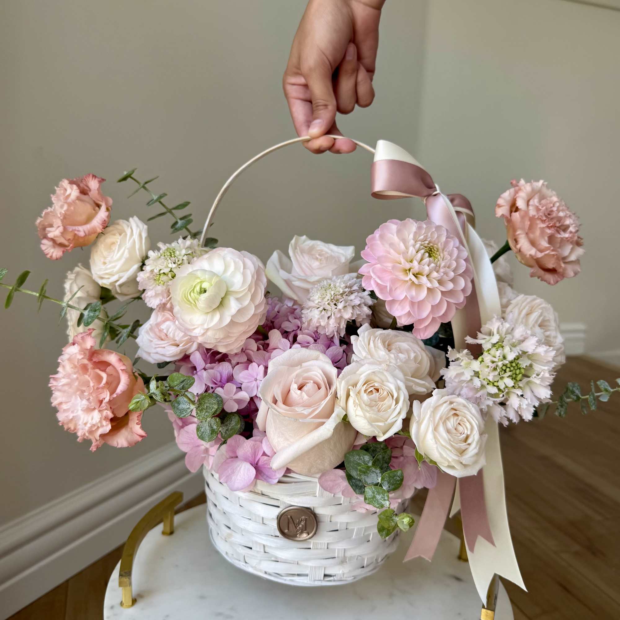 Pastel flower arrangement in a white basket with a ribbon handle