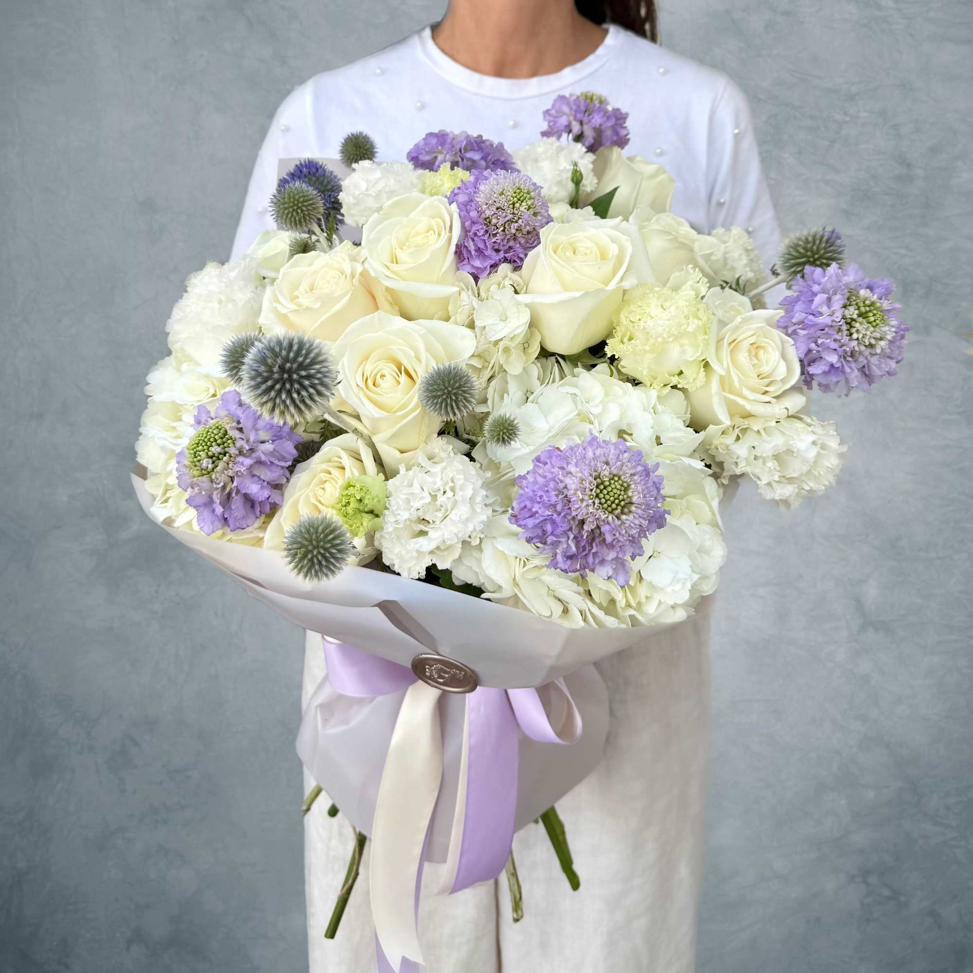 Large bouquet of white roses and lavender flowers wrapped in pale paper