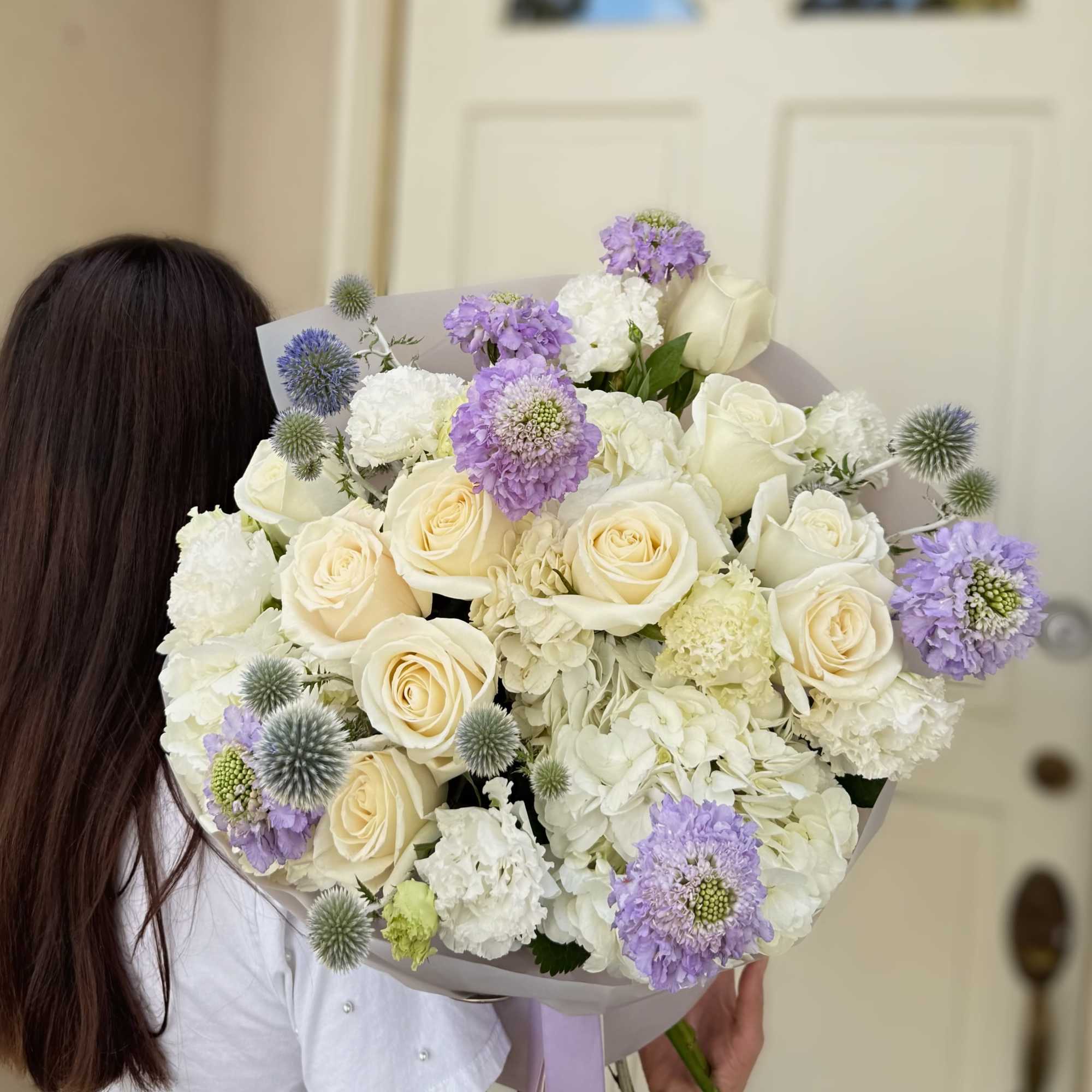 Bouquet of cream roses, white blooms, and lavender flowers wrapped in paper