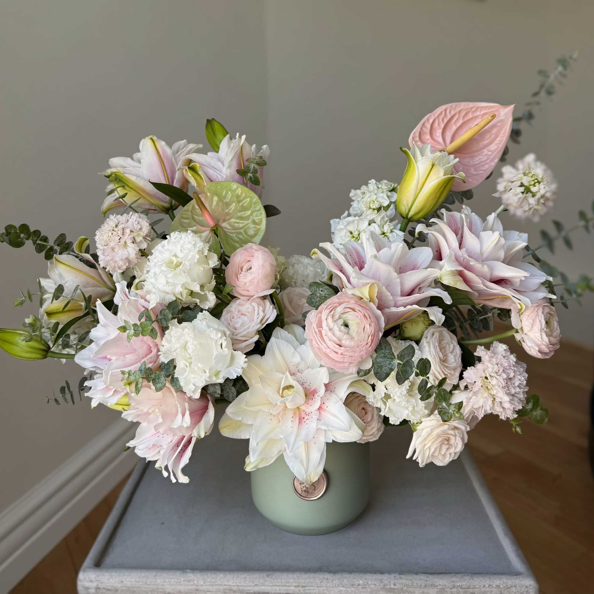 Pastel bouquet of lilies, roses, and anthurium in a green vase