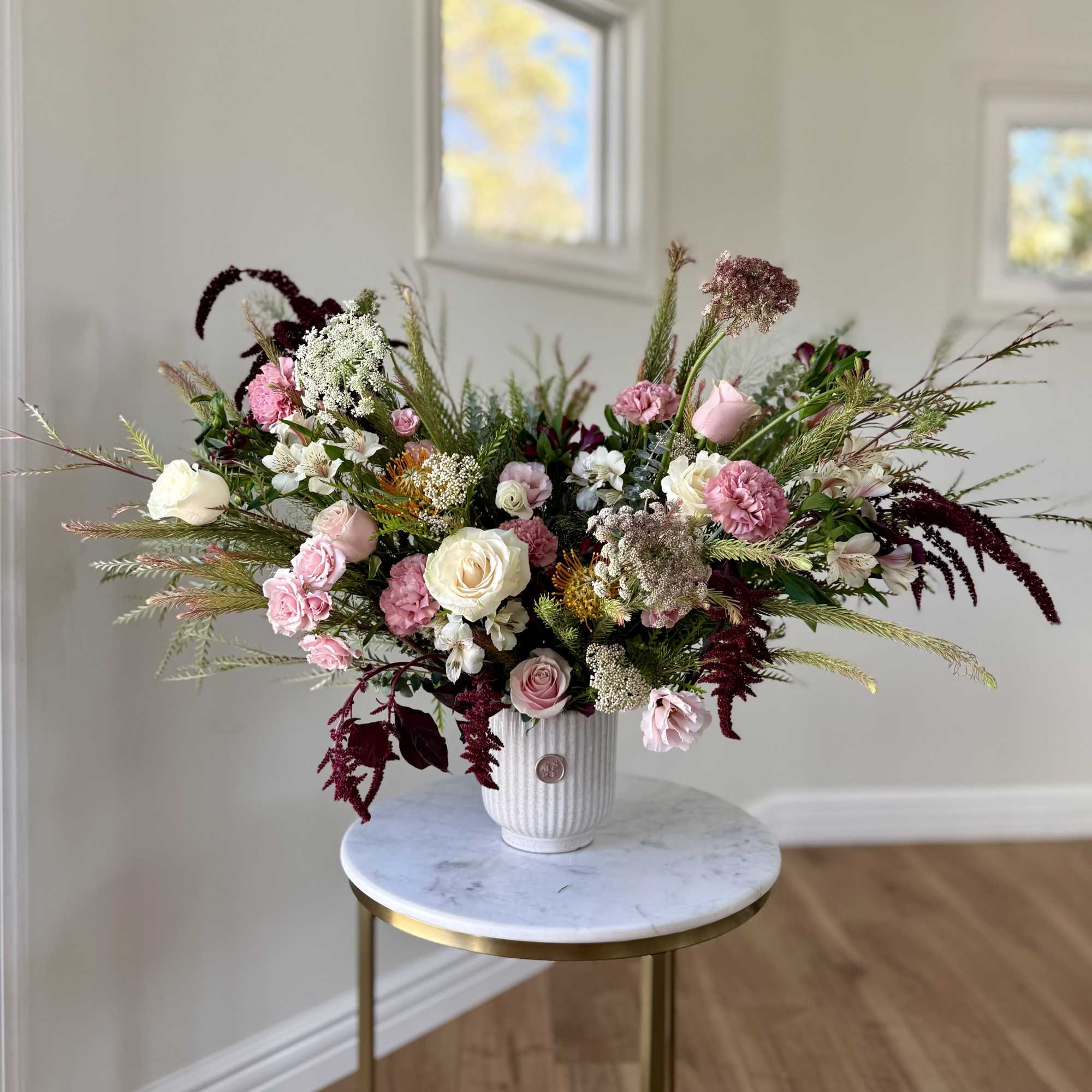 Large mixed flower arrangement in a white vase on a small round table