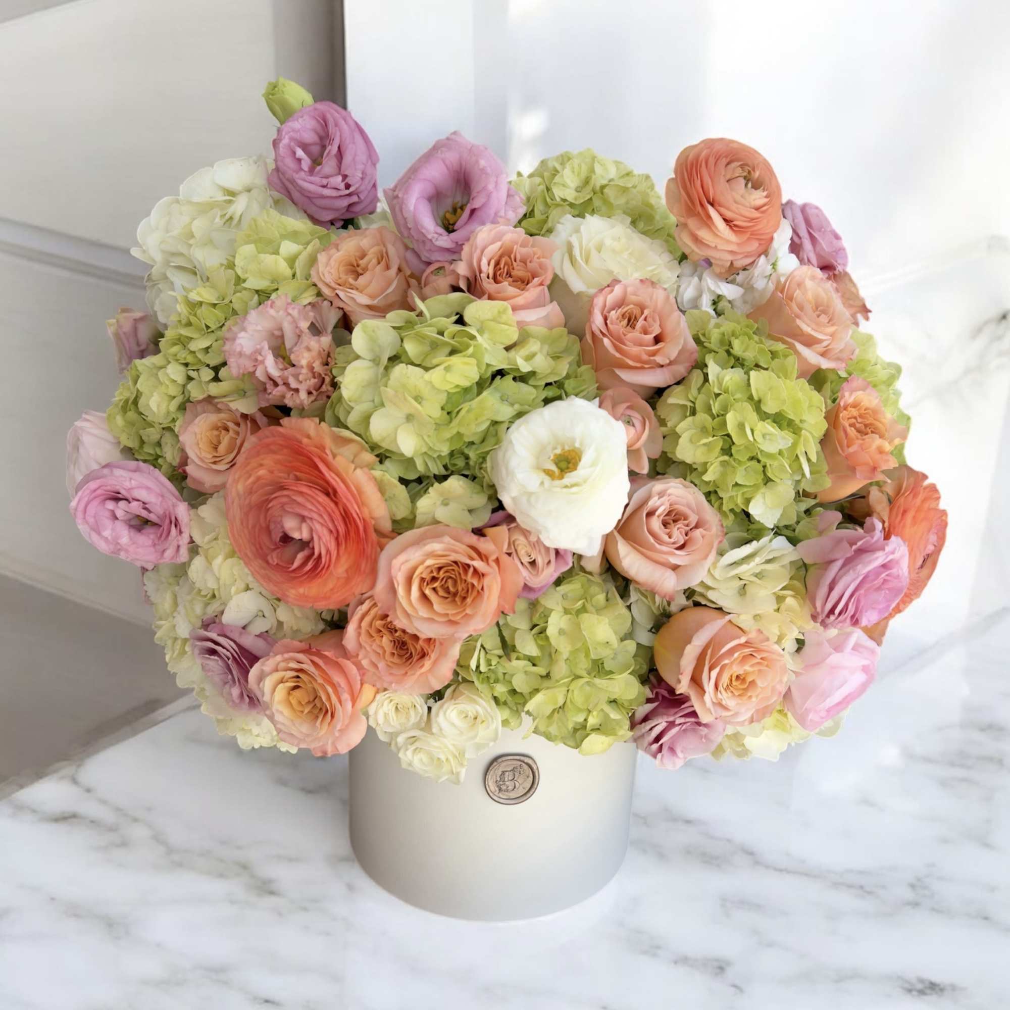 Pastel bouquet of roses, ranunculus, and hydrangeas in a white hat box