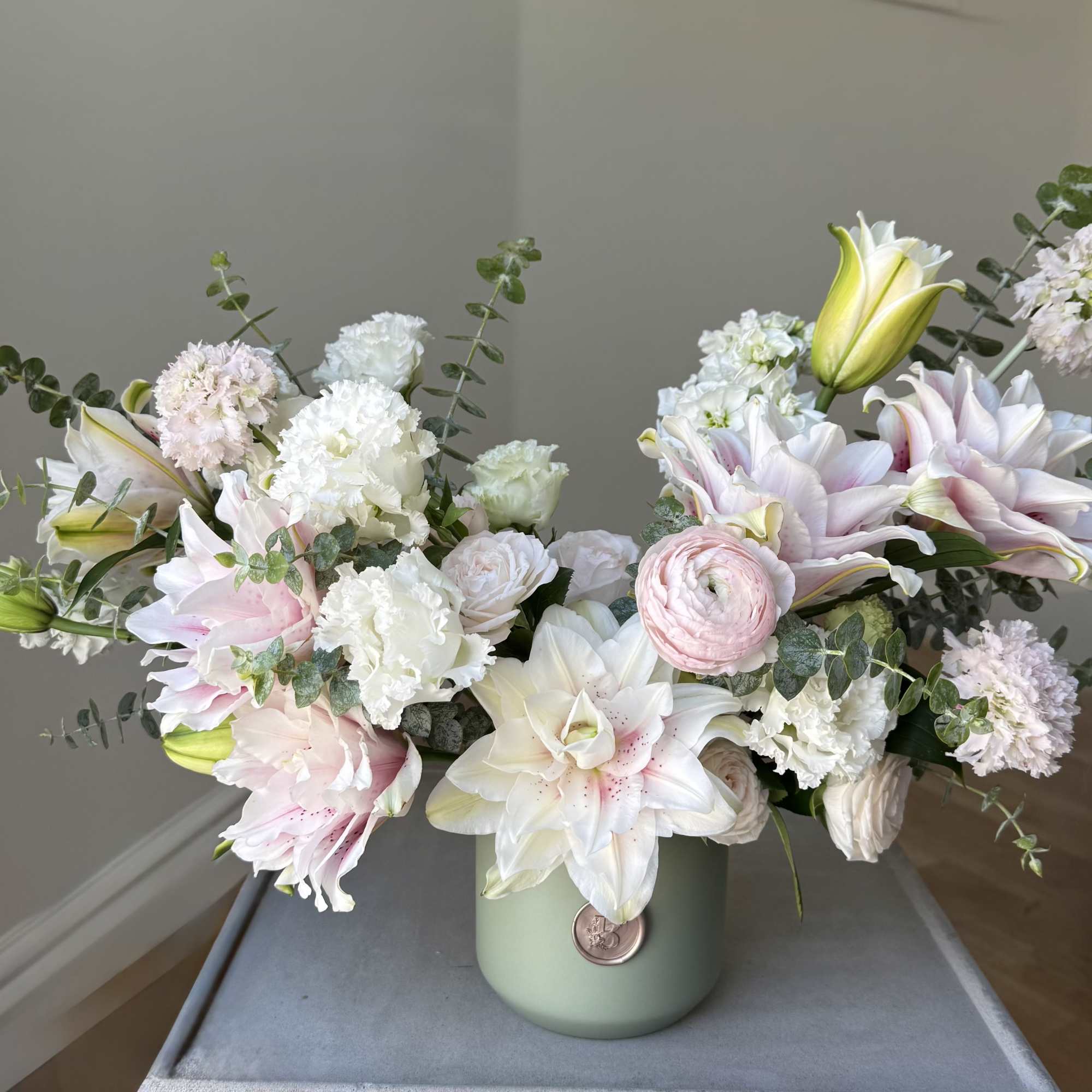 Pastel bouquet of lilies, carnations, and ranunculus in a green vase