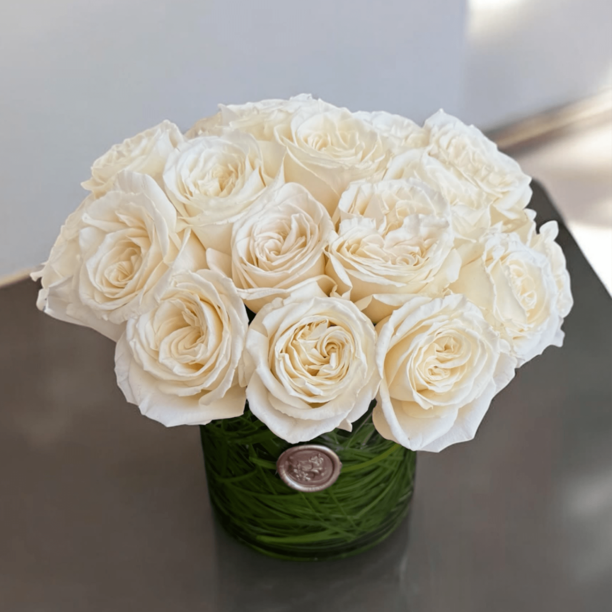 Twenty-four beautiful roses arranged in a clear glass vase. A classic and