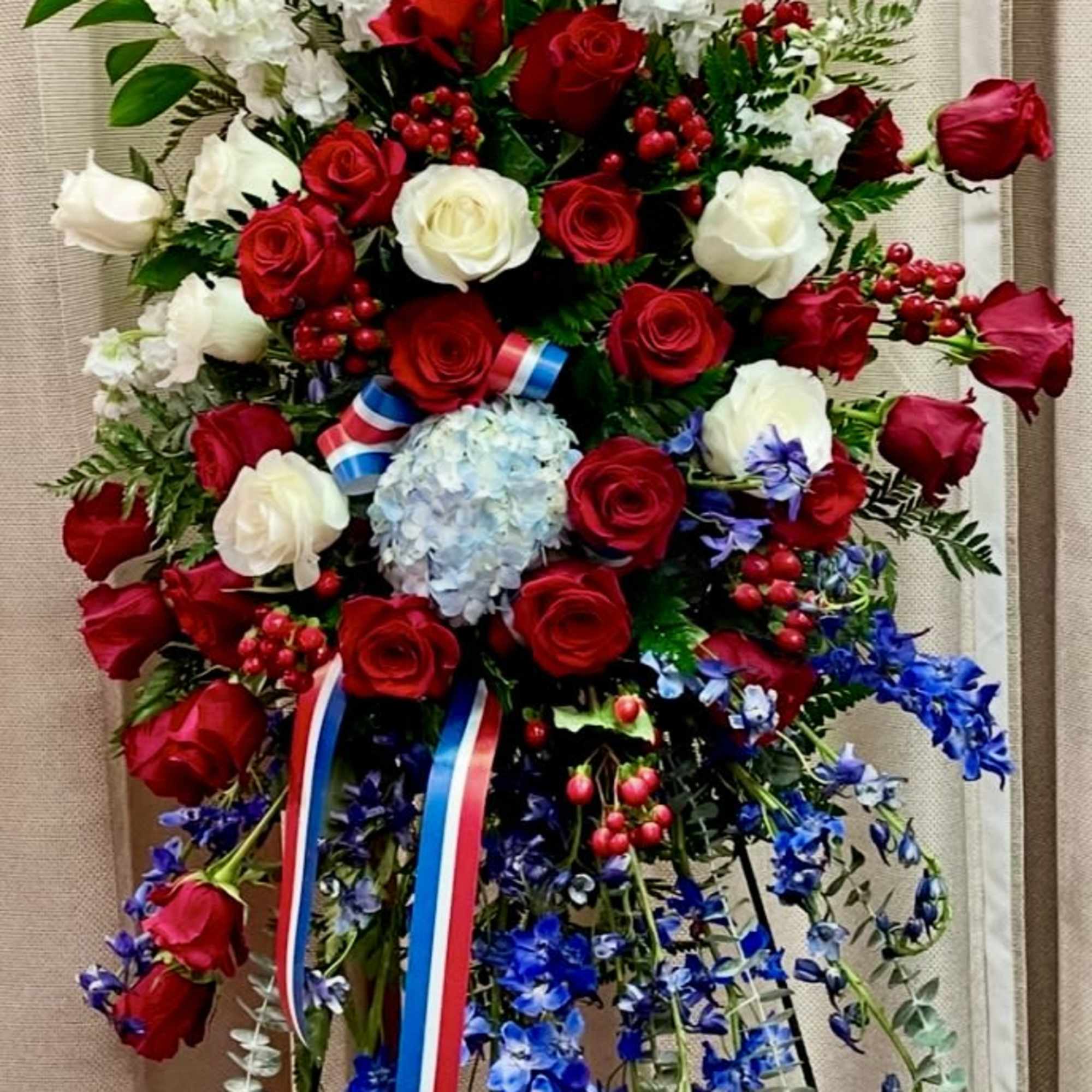 Tall standing floral spray with red and white roses, white blooms, and blue hanging flowers