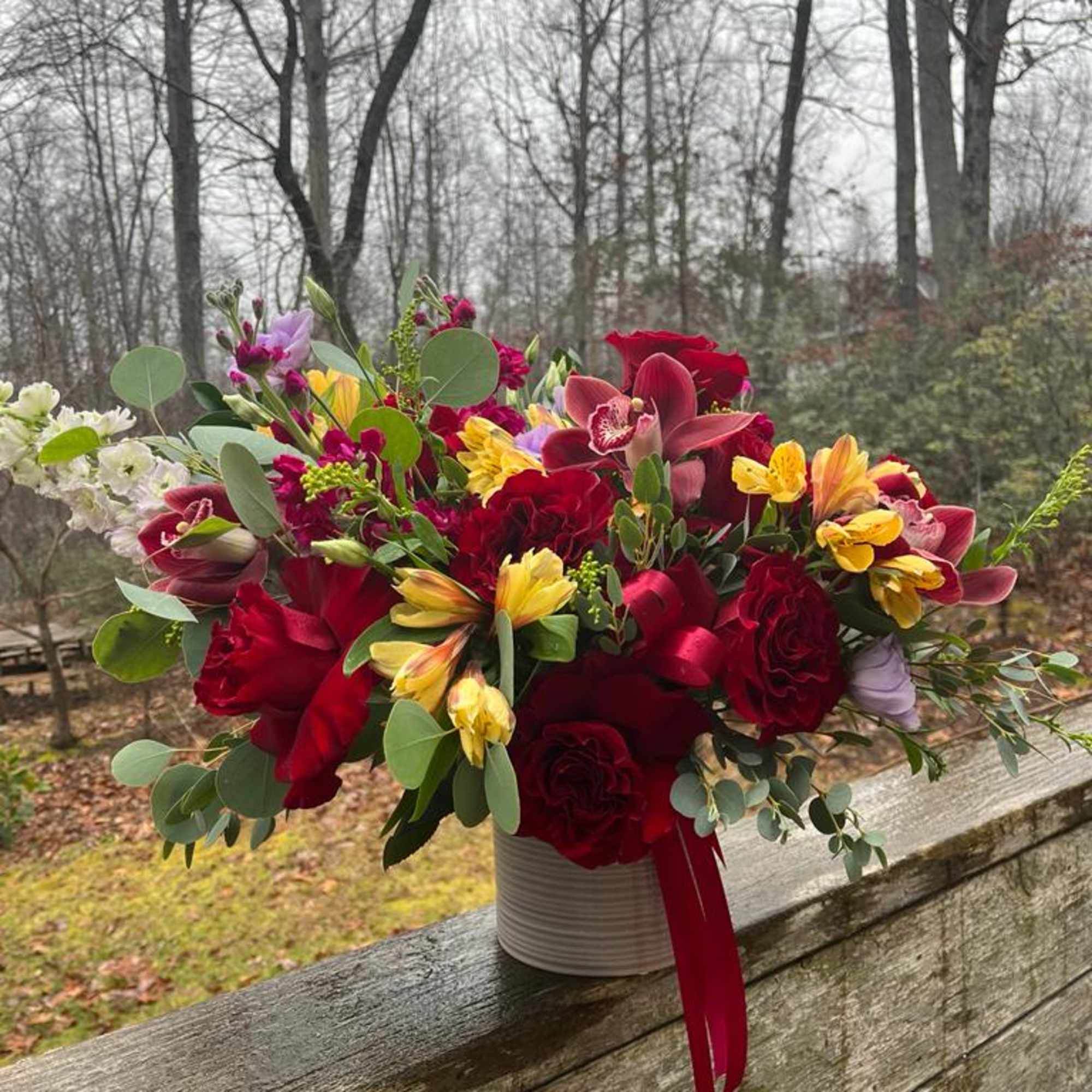 Mixed bouquet of red, yellow, and pink flowers in a white container