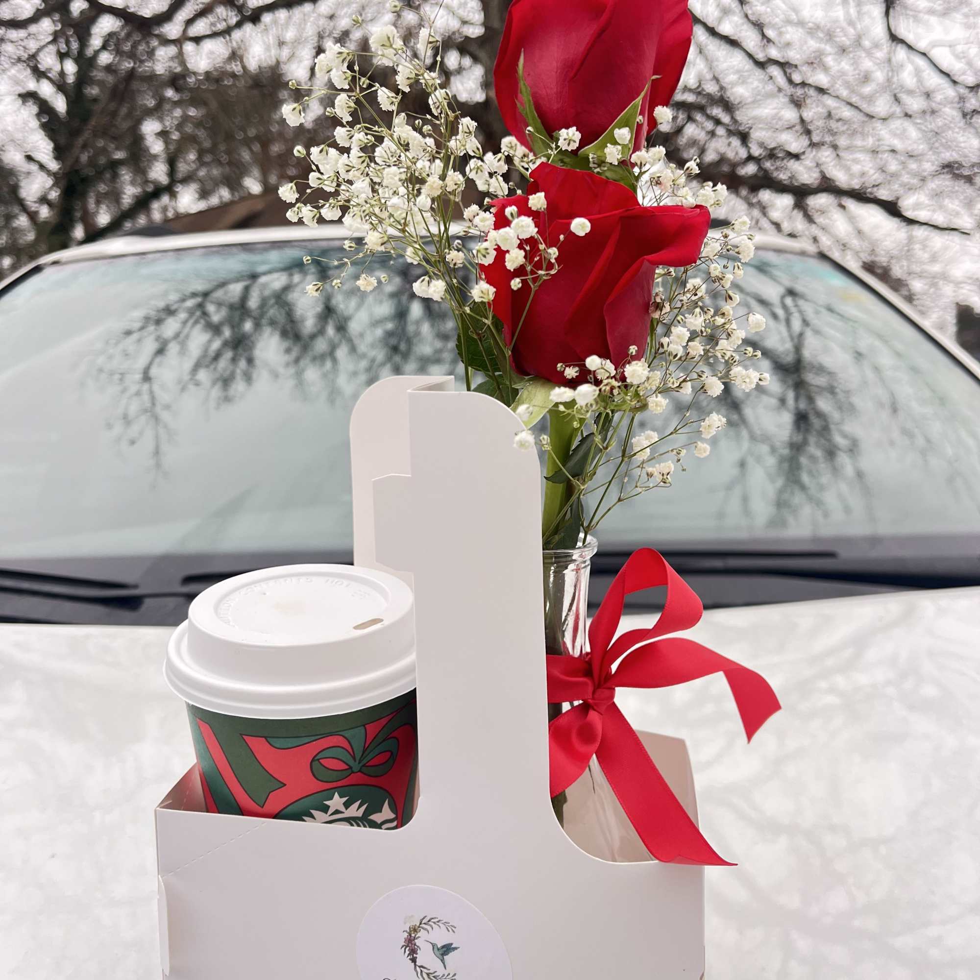 Two red roses in a small vase with baby's breath and a coffee cup in a gift box