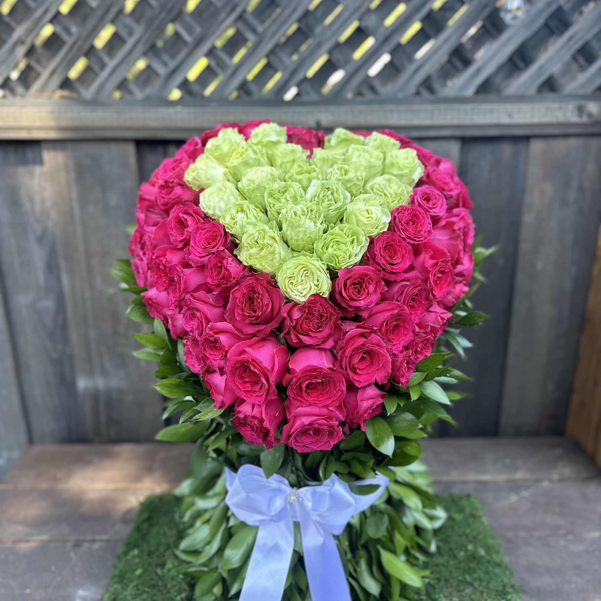 Heart-shaped rose arrangement in hot pink and lime green with a blue ribbon