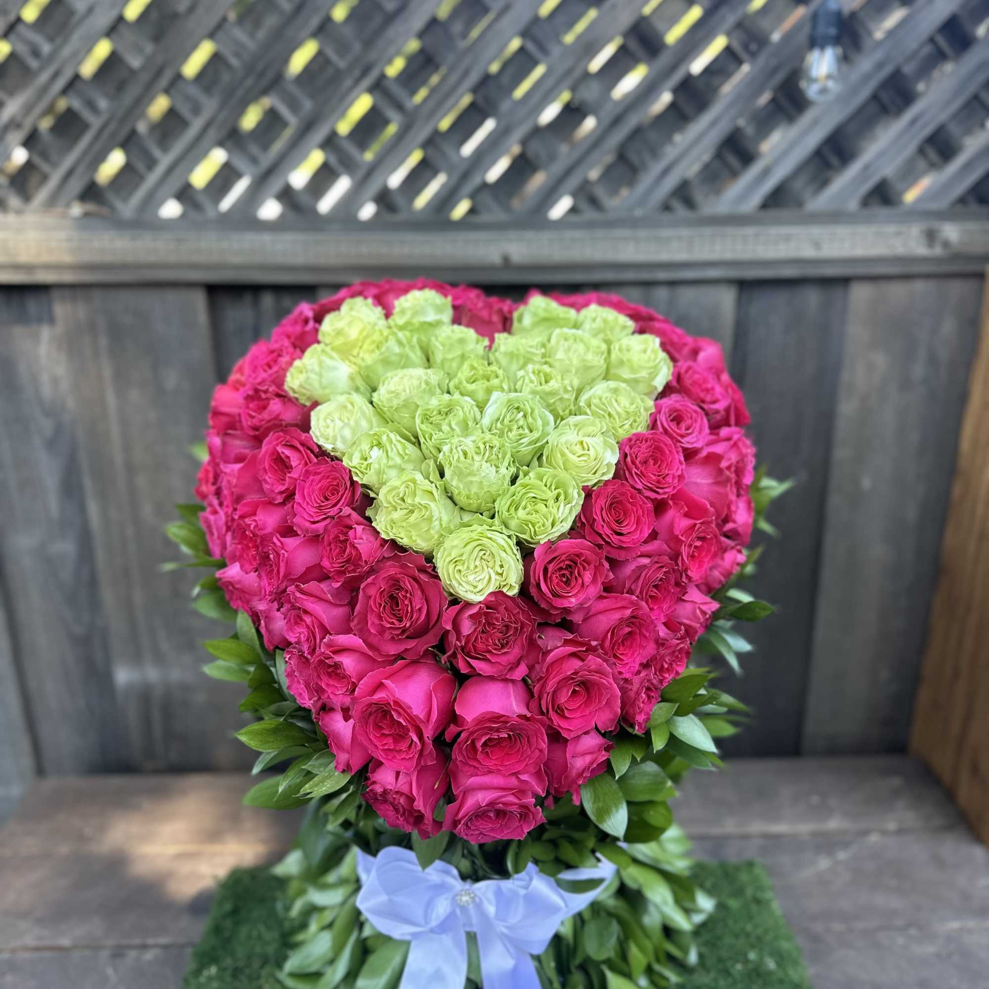 Heart-shaped rose arrangement in pink and green with a blue ribbon