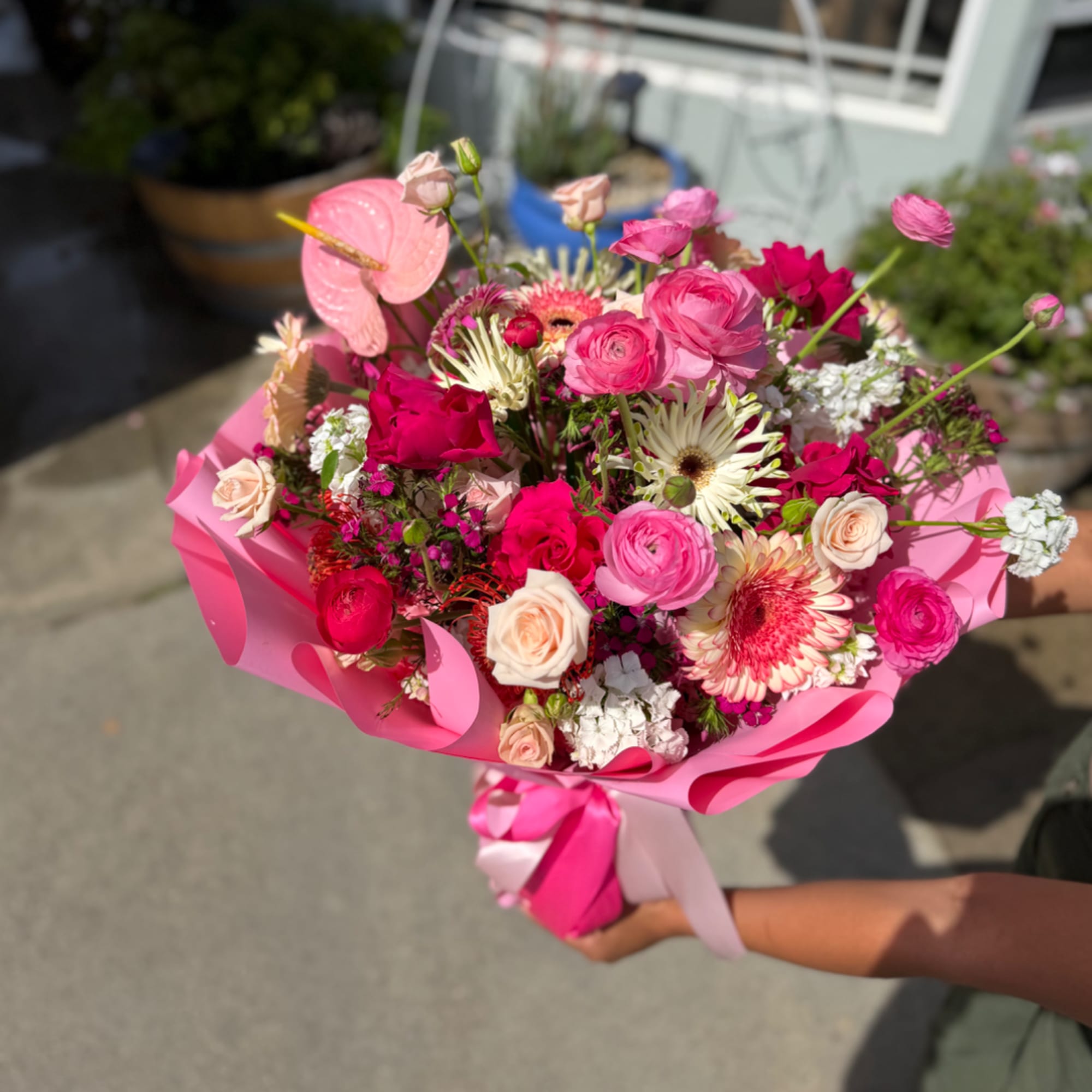 Handheld bouquet of pink and white mixed flowers wrapped in bright pink paper