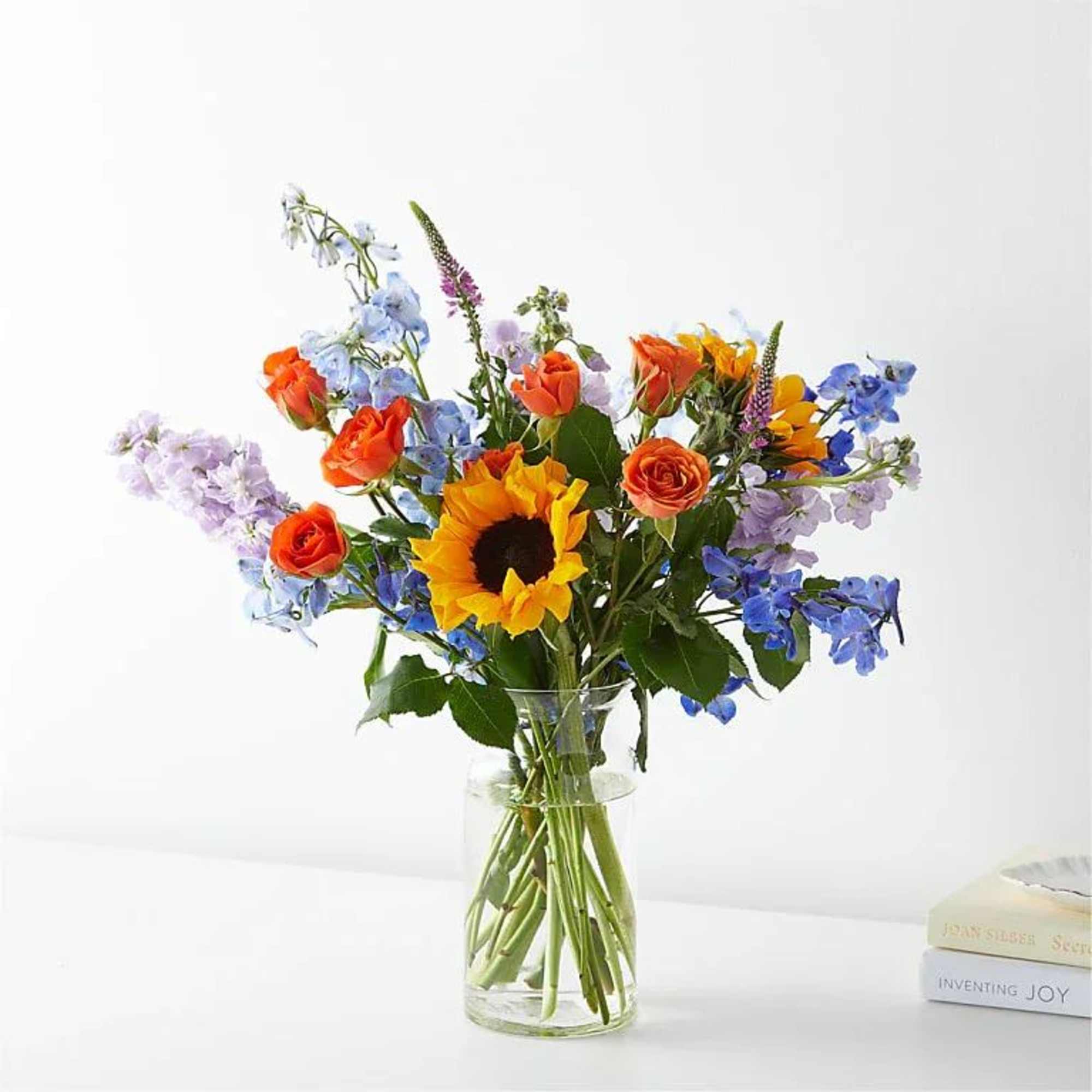 Mixed bouquet with sunflowers, orange roses, and blue flowers in a glass vase