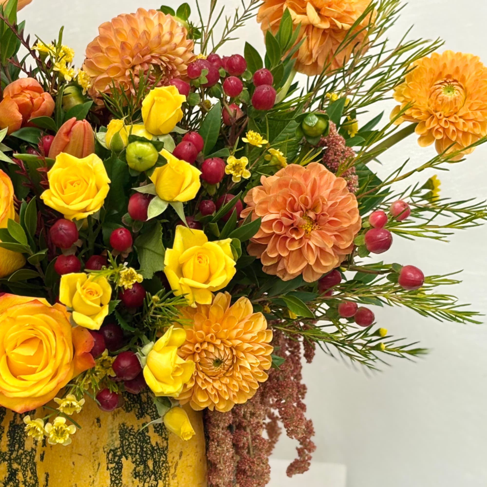 Yellow roses and orange dahlias in a vase with red berries