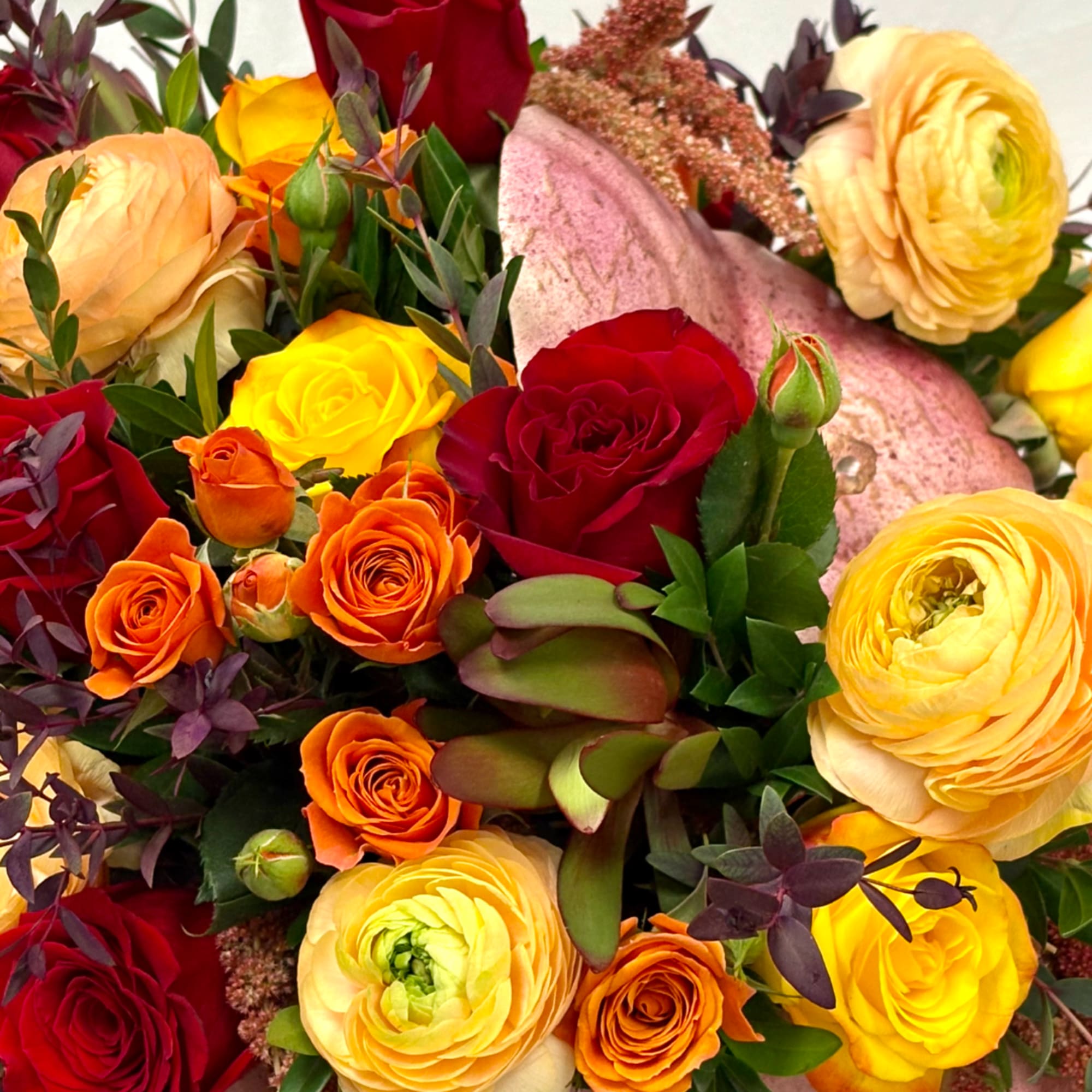 Mixed bouquet of roses and ranunculus in red, yellow, orange, and blush tones