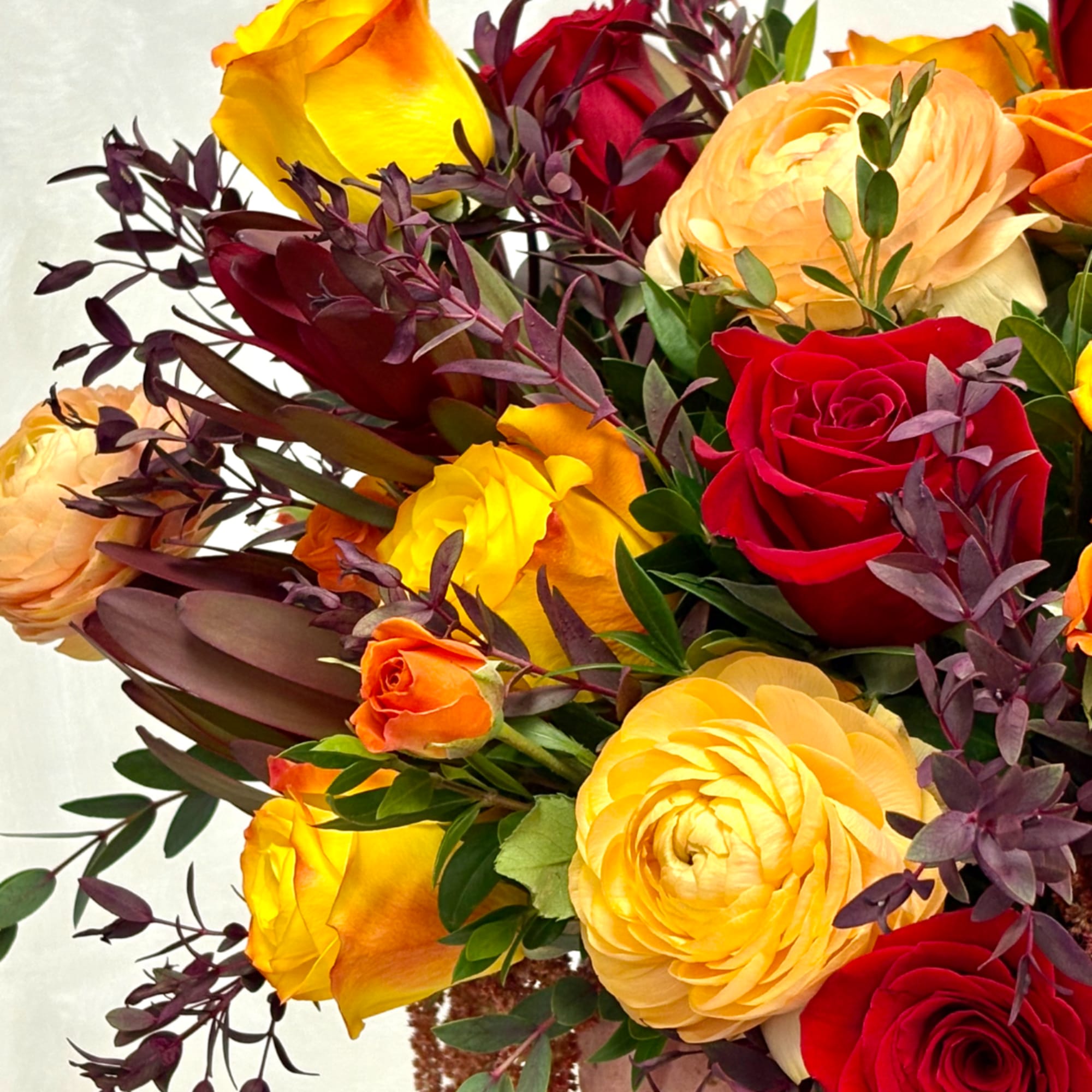 Bouquet of red, yellow, and peach roses with dark foliage