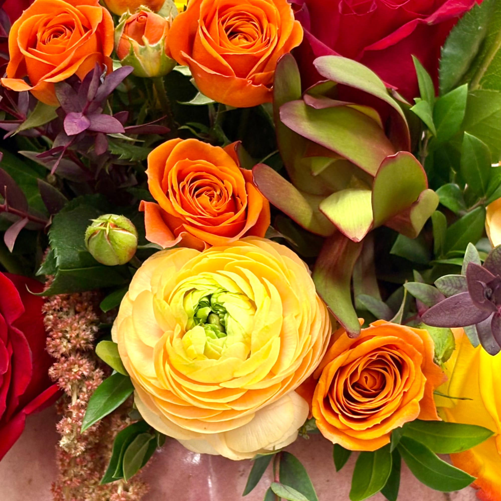 Bouquet of orange roses and yellow ranunculus with mixed foliage