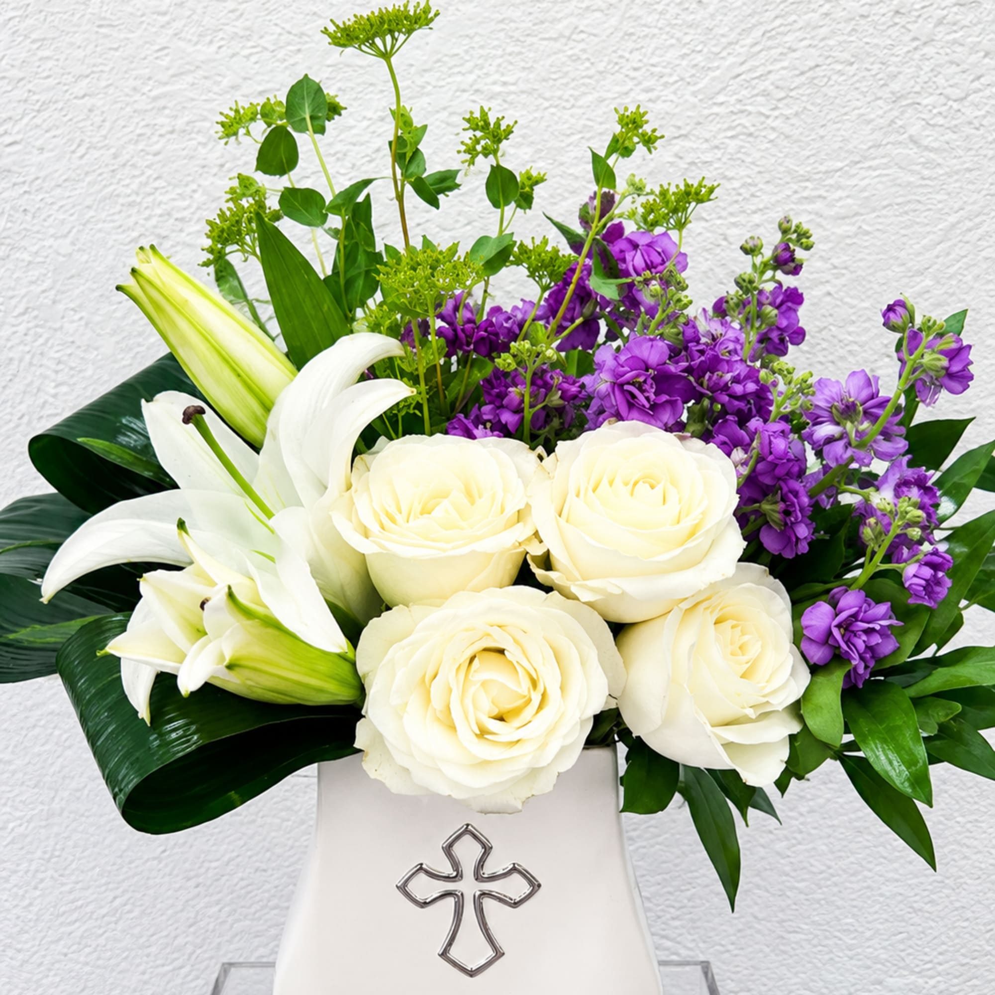 White roses and lilies arranged in a white vase with purple flowers