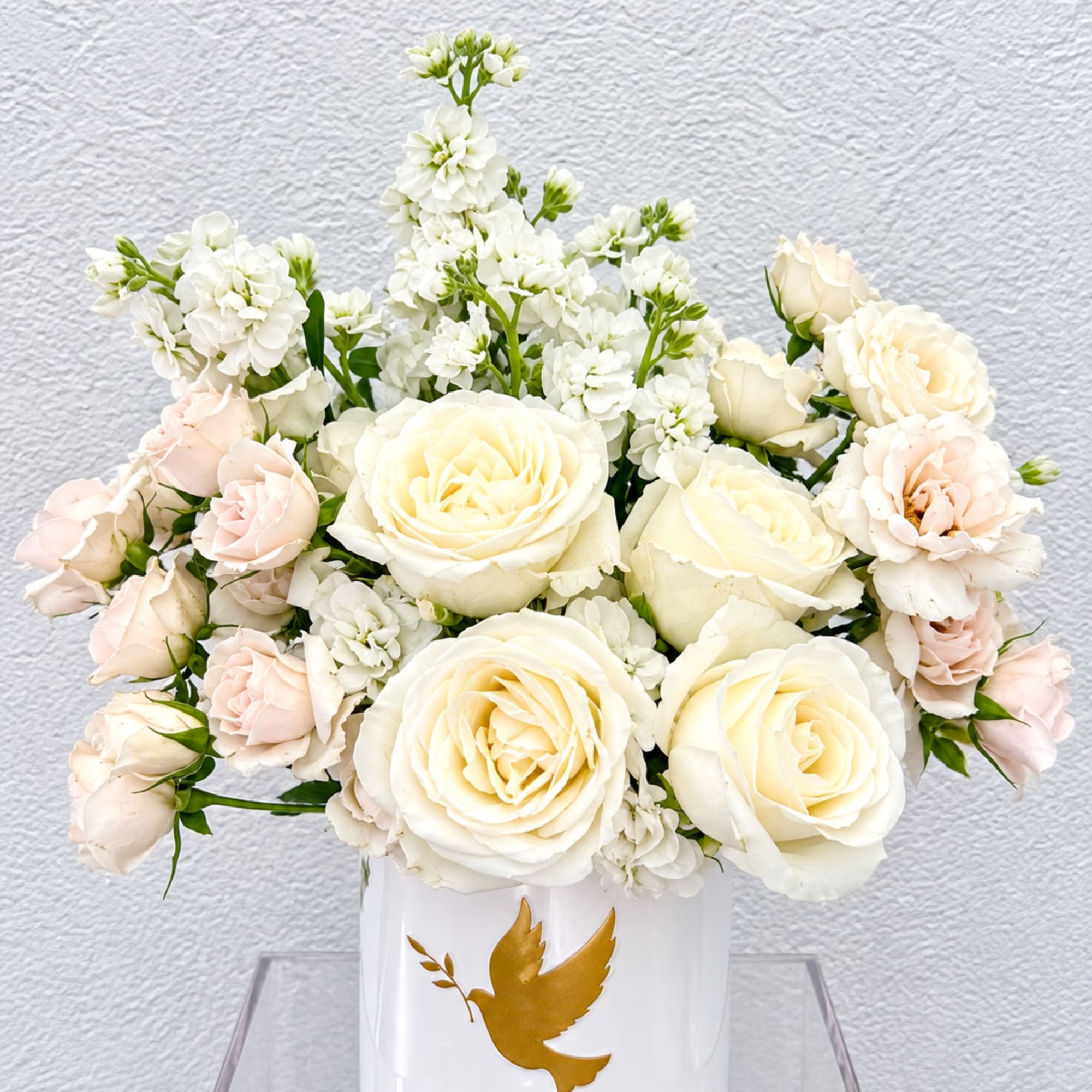 White and blush roses arranged in a white vase with a gold dove emblem