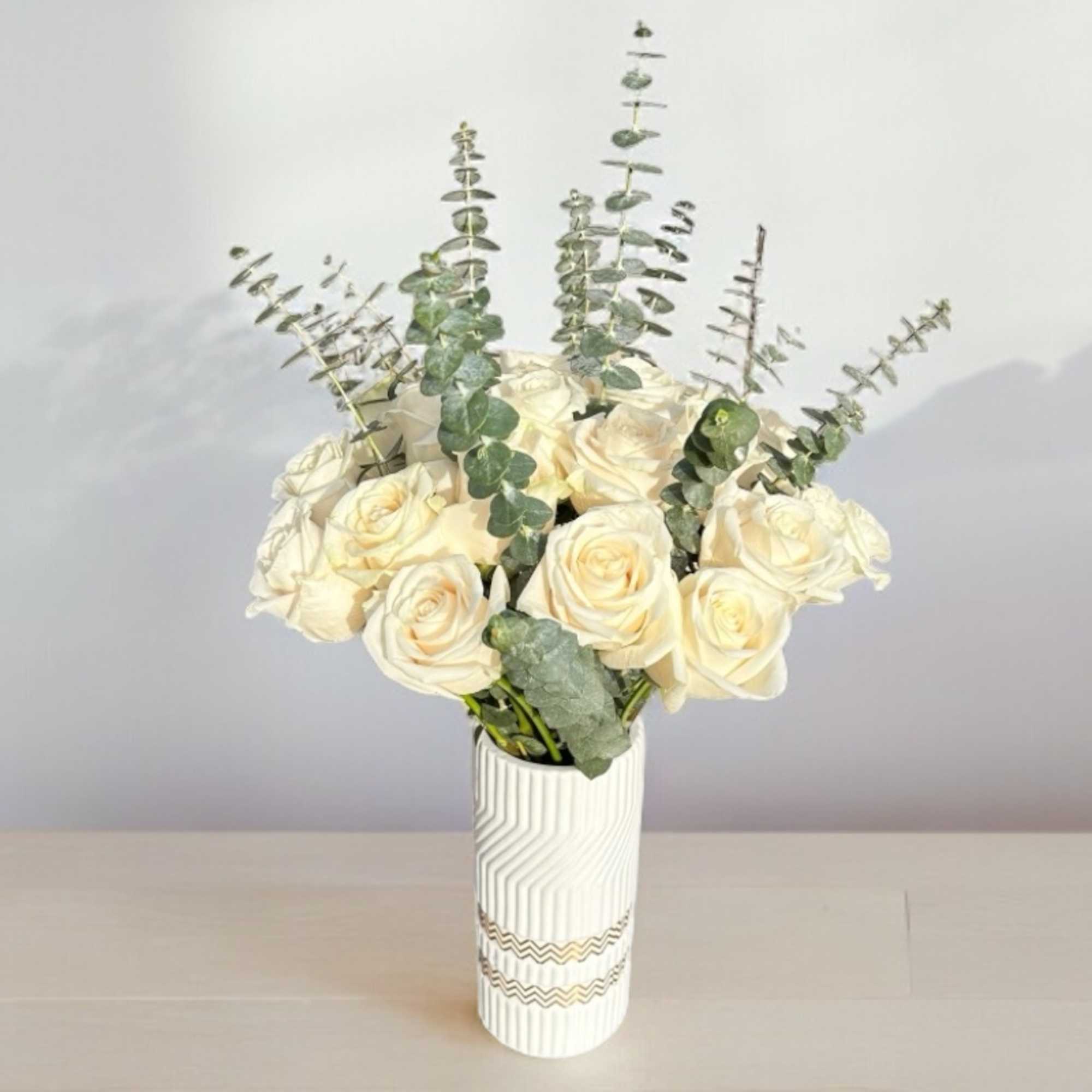 White rose bouquet in a patterned vase with eucalyptus stems