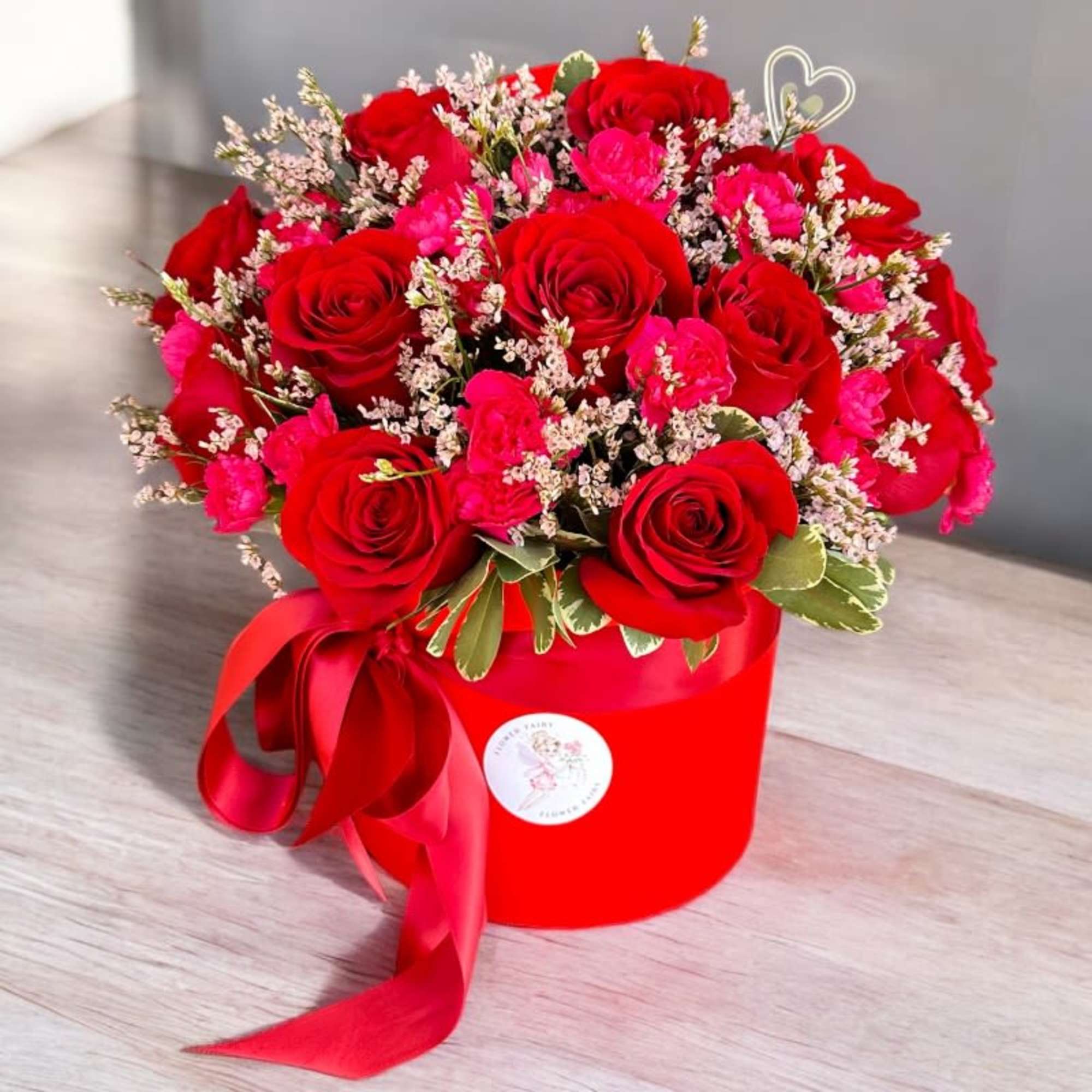 Red roses and pink carnations in a red hatbox with ribbon