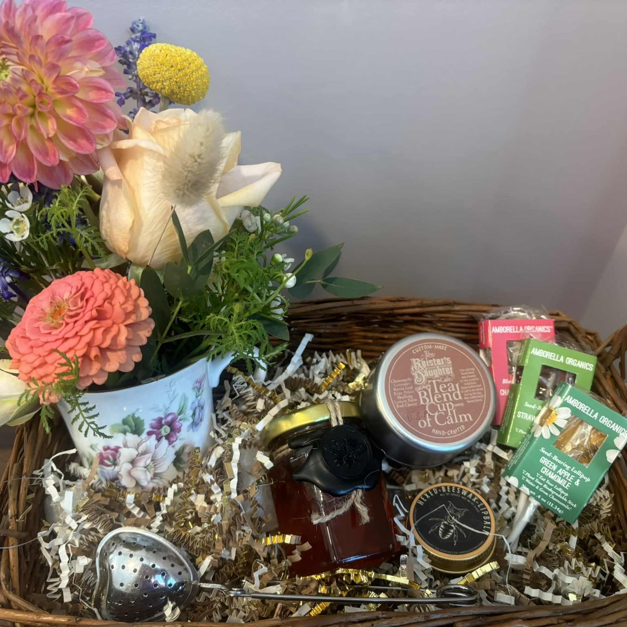 A basket filled with flowers, tea, and treats.  The flower arrangement