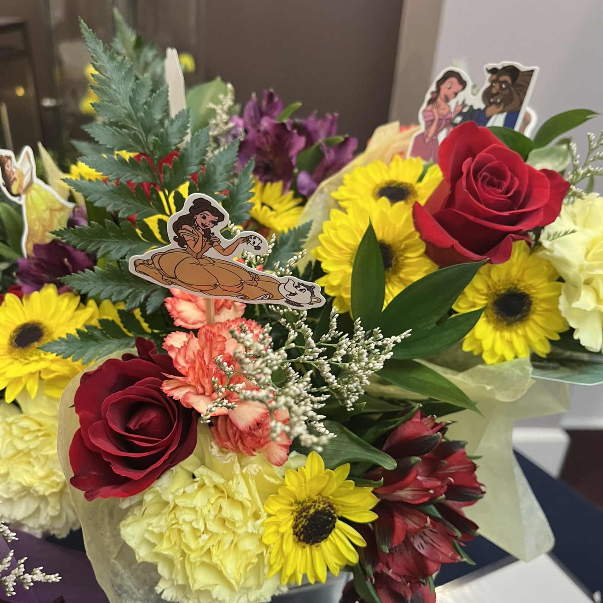 Mixed bouquet with red roses, yellow daisies, and carnations in a black container