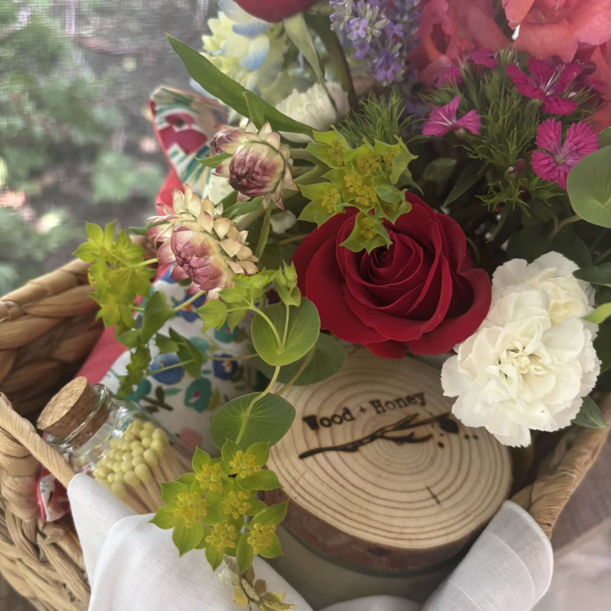 Basket arrangement with red roses, pink blooms, and white carnations