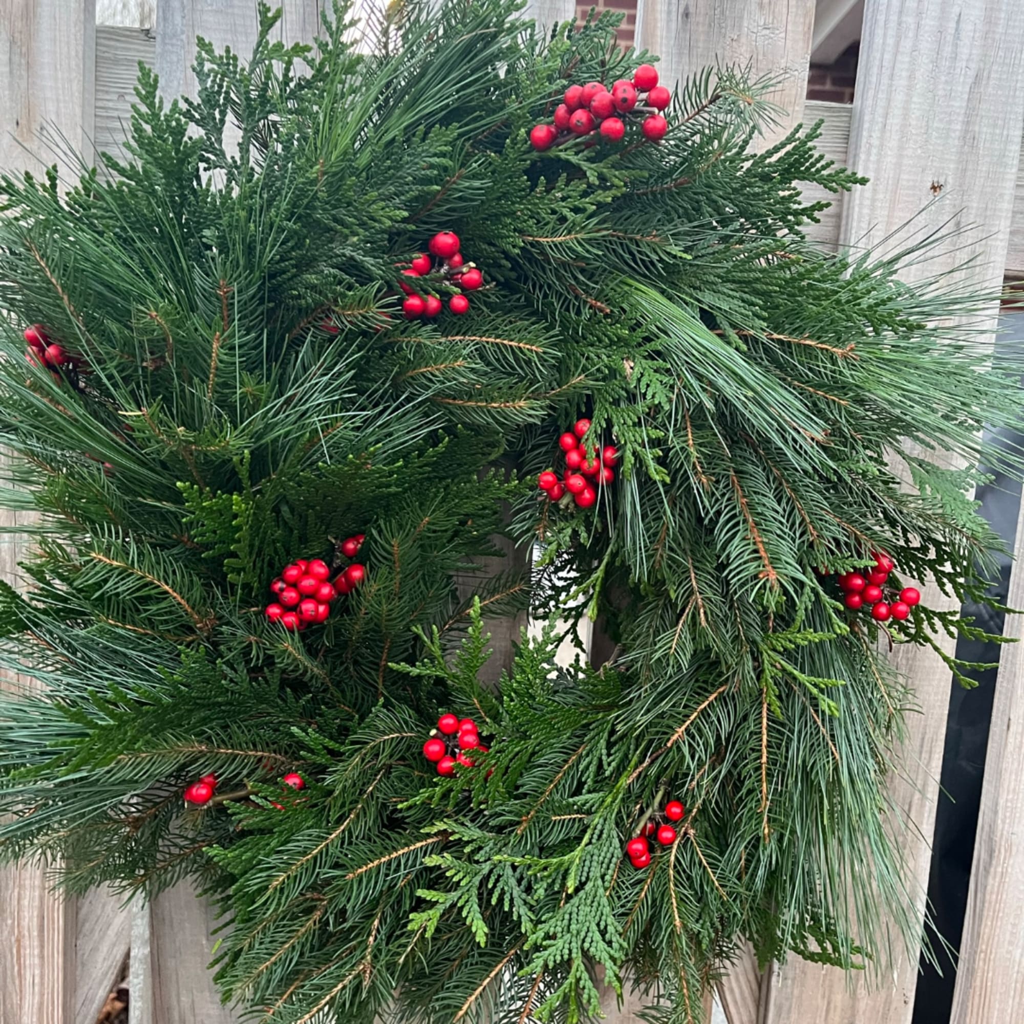 Evergreen wreath with red berries hanging on a wooden fence