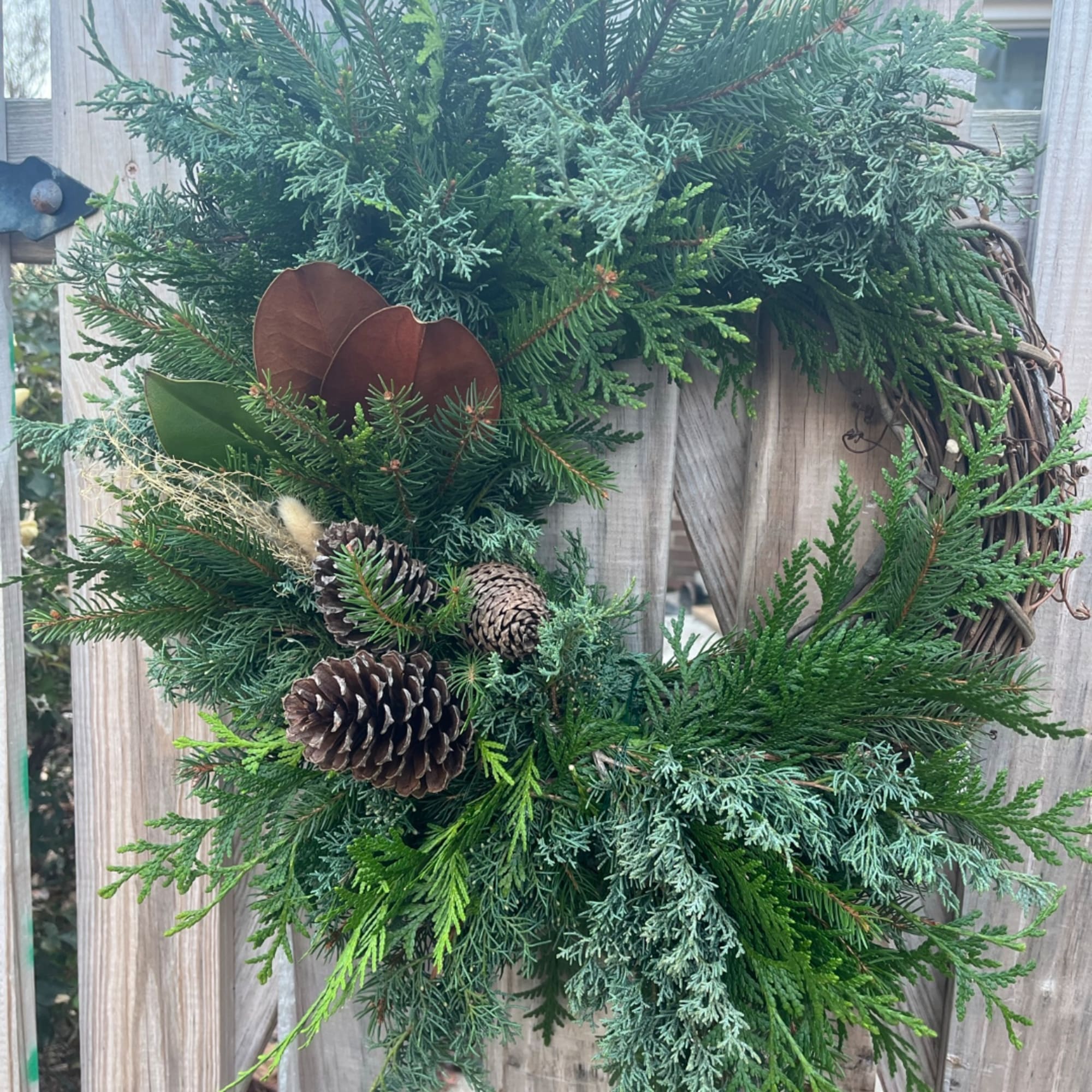 Evergreen wreath with pinecones and brown seed pods on a grapevine base