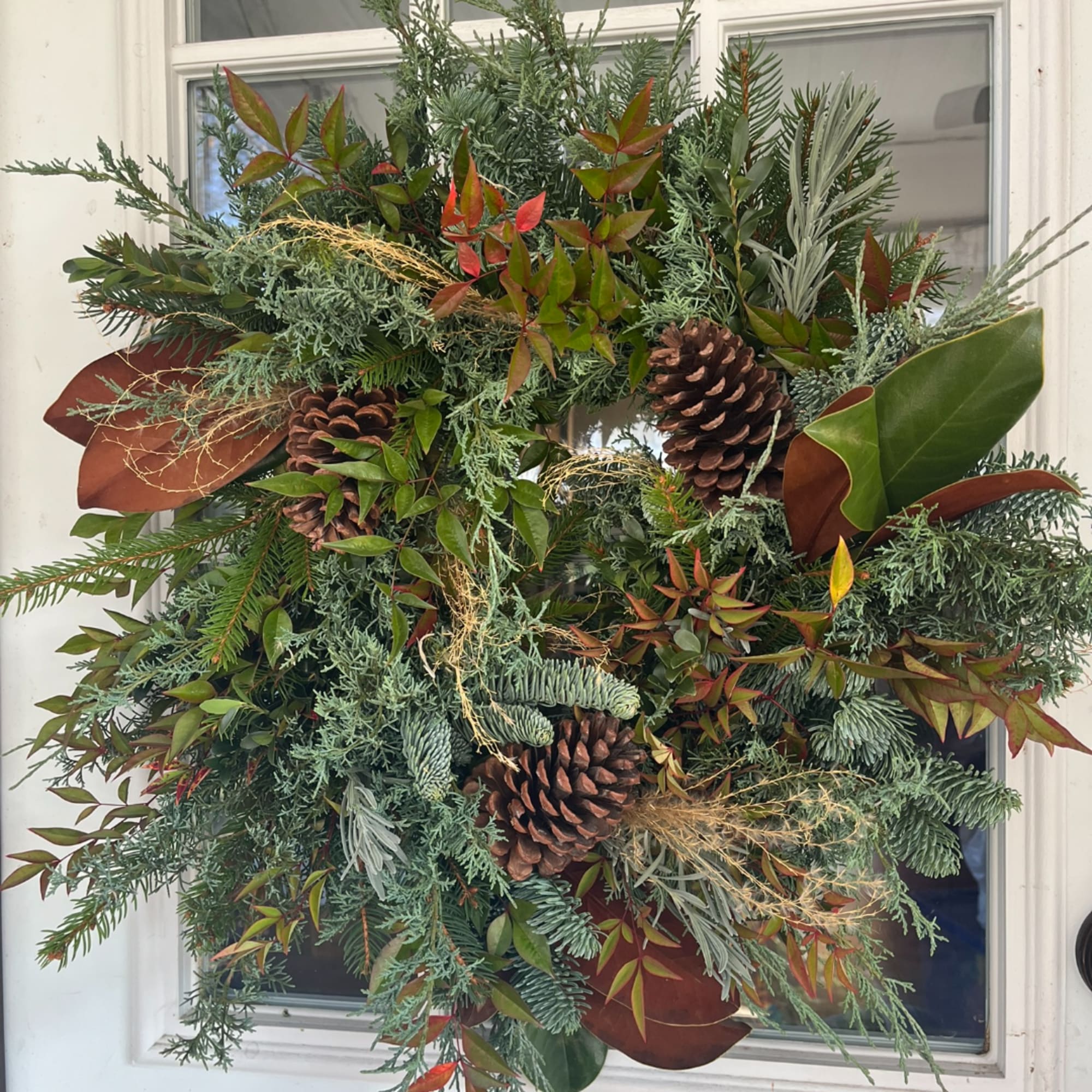 Large evergreen wreath with pinecones and mixed foliage on a white door