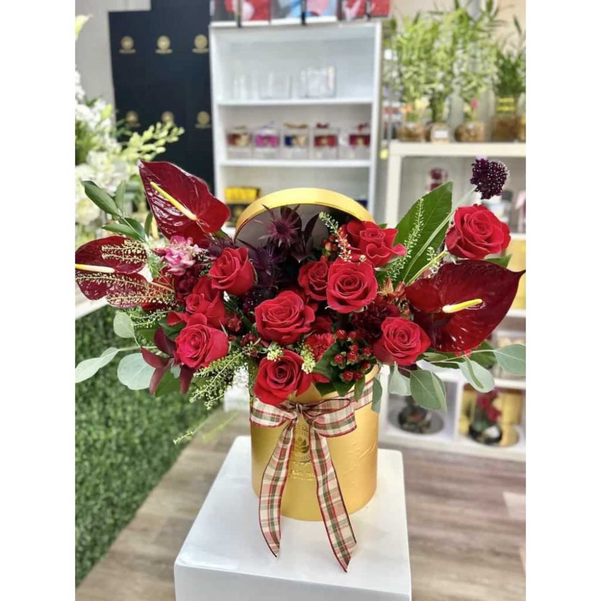 Red roses and red tropical flowers in a yellow hatbox with a plaid ribbon bow