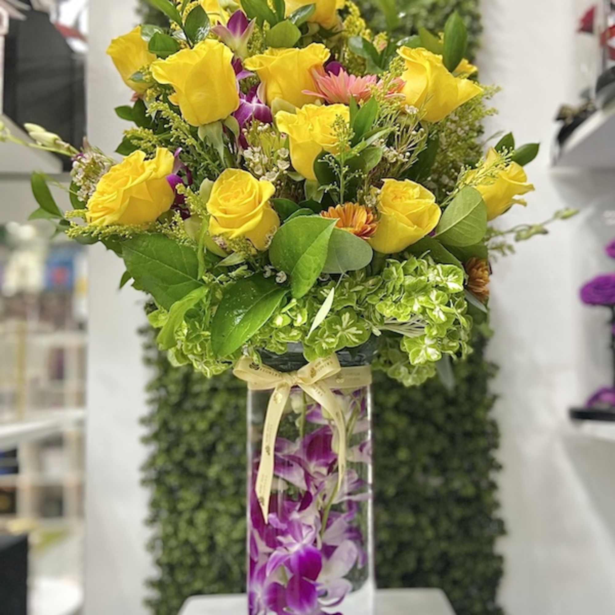 Tall glass vase with yellow roses and submerged purple orchids in a layered arrangement.