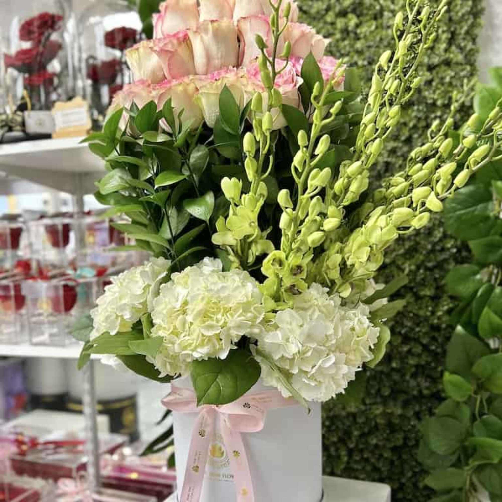 Tall hatbox arrangement with pink-tipped roses, white hydrangeas, and green orchids in a white box with pink ribbon
