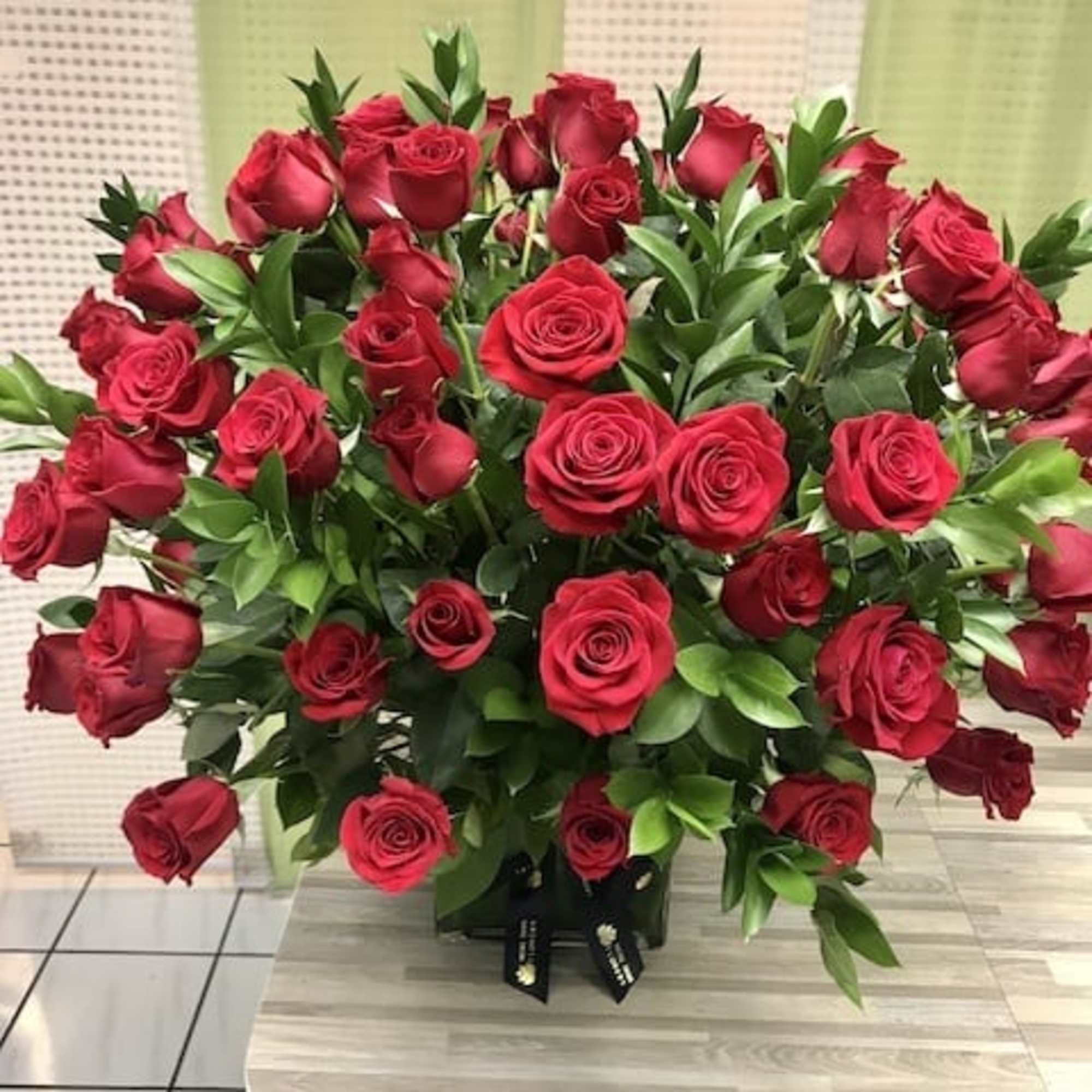 Large arrangement of red roses in a black square vase on a countertop
