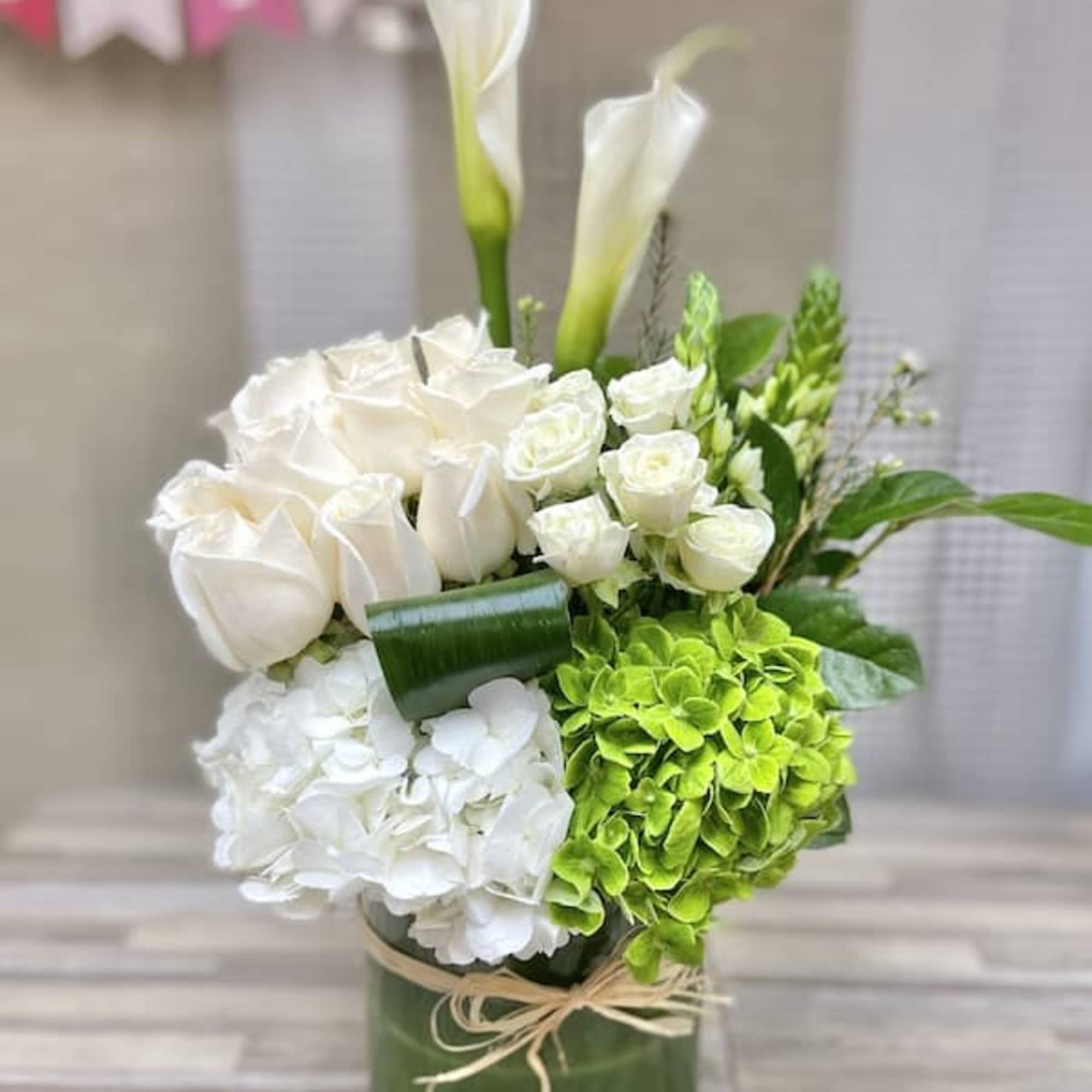 Tall white and green arrangement with calla lilies, roses, and hydrangeas in a glass cylinder vase