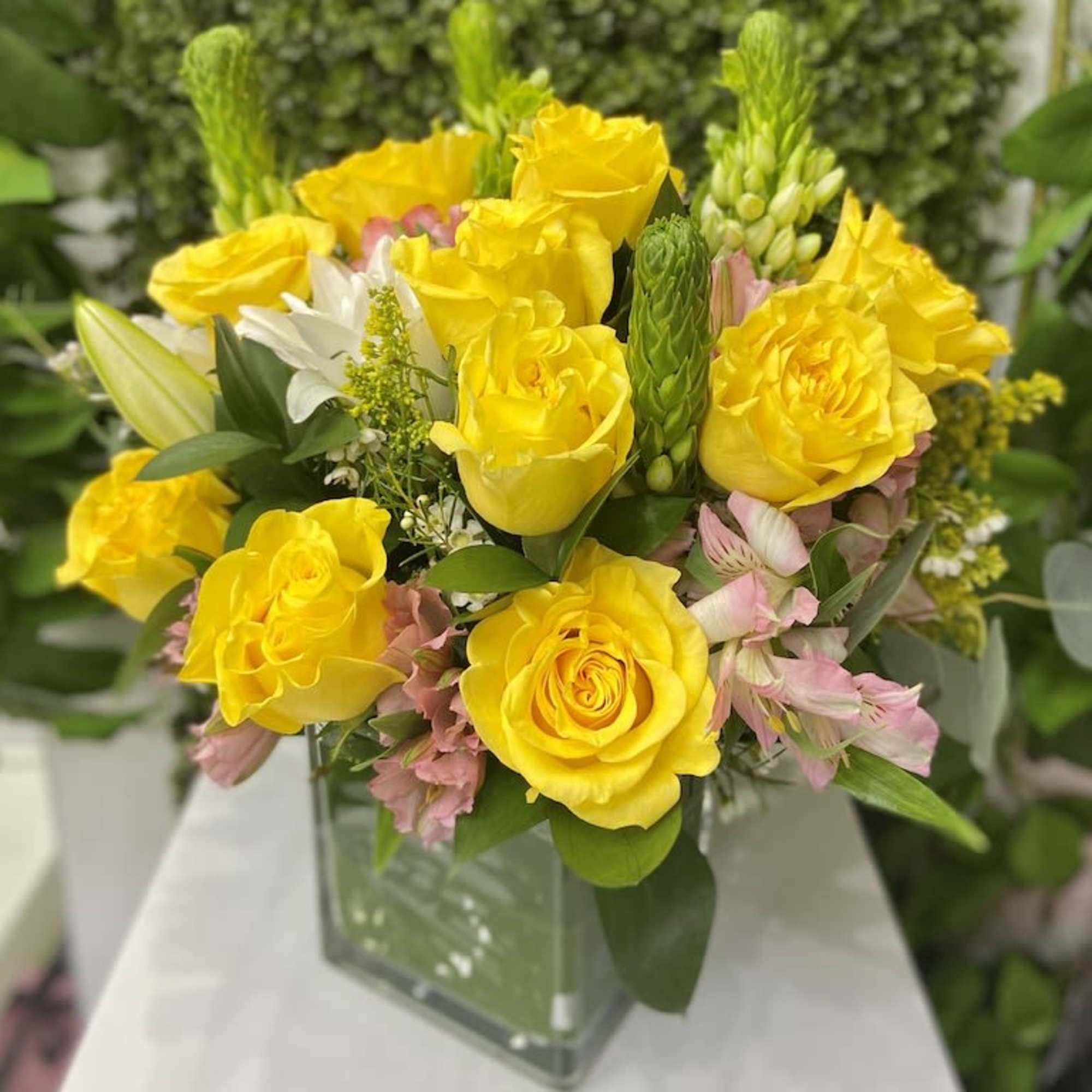 Yellow rose and pink alstroemeria arrangement with white lilies in a square glass vase