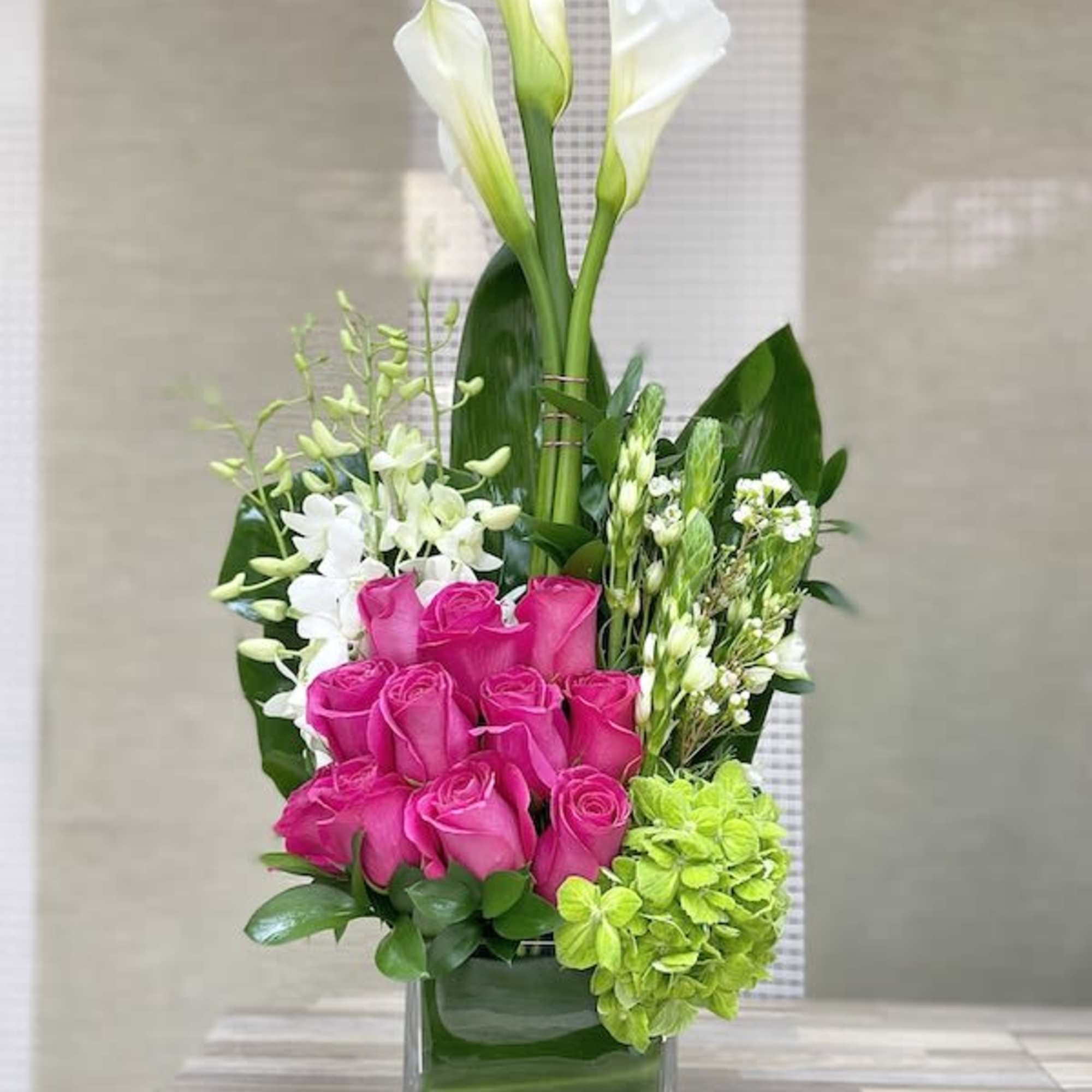 Tall arrangement of white calla lilies, pink roses, white orchids and green hydrangea in a glass vase