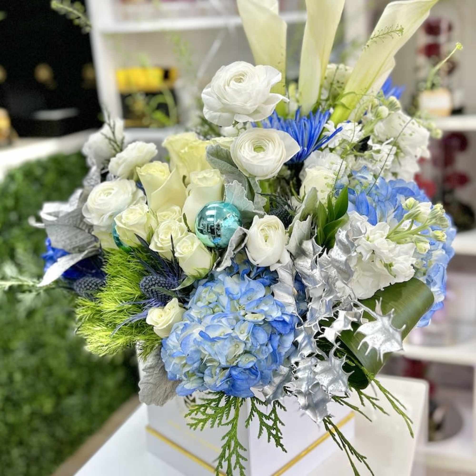 White and blue flower arrangement with calla lilies, roses, and hydrangeas in a white box with silver accents.