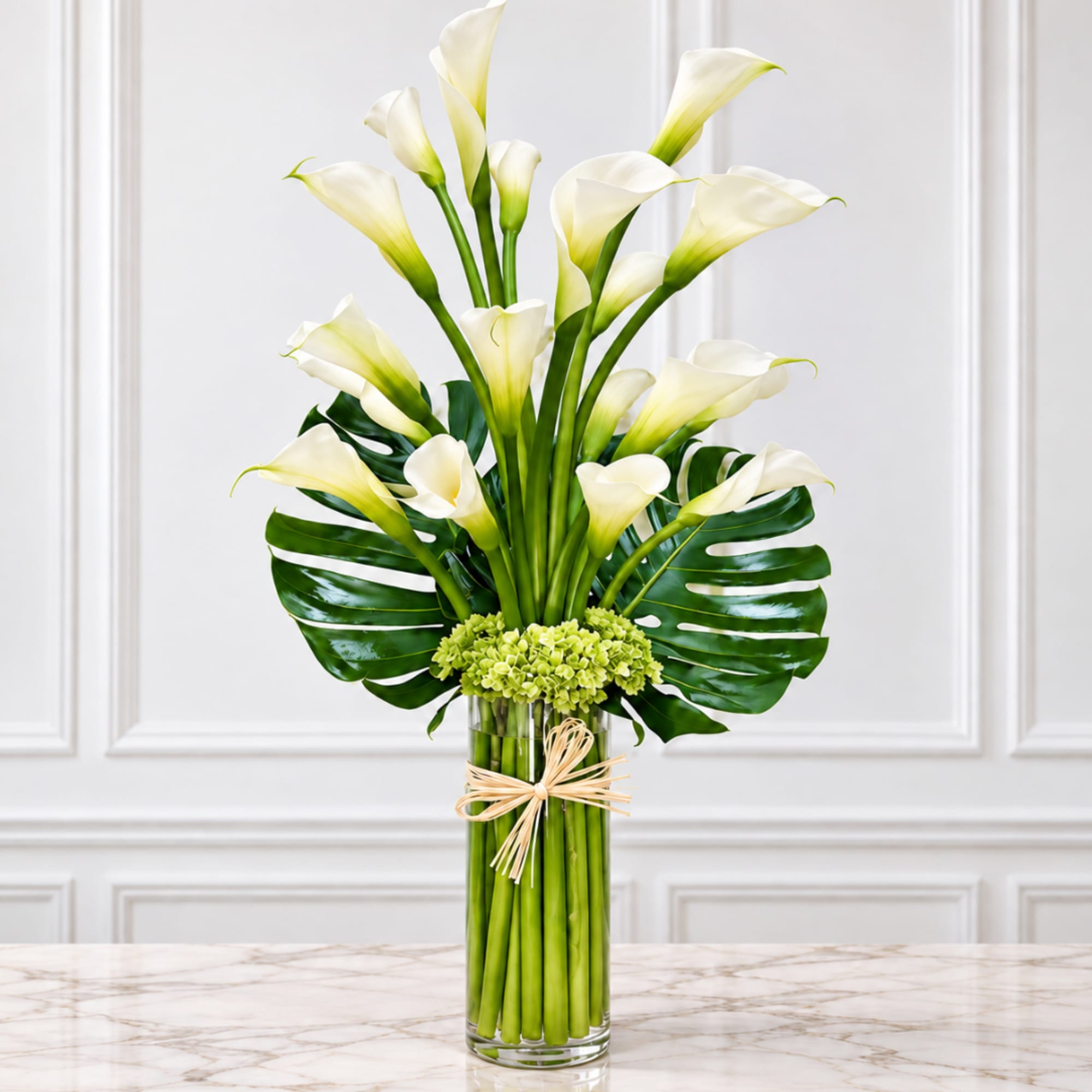 White calla lilies in a tall glass vase with green tropical leaves