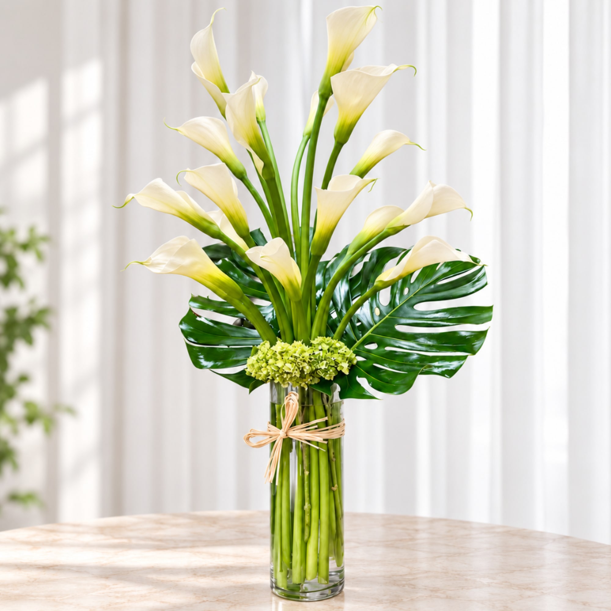 White calla lilies arranged in a tall glass vase with tropical leaves